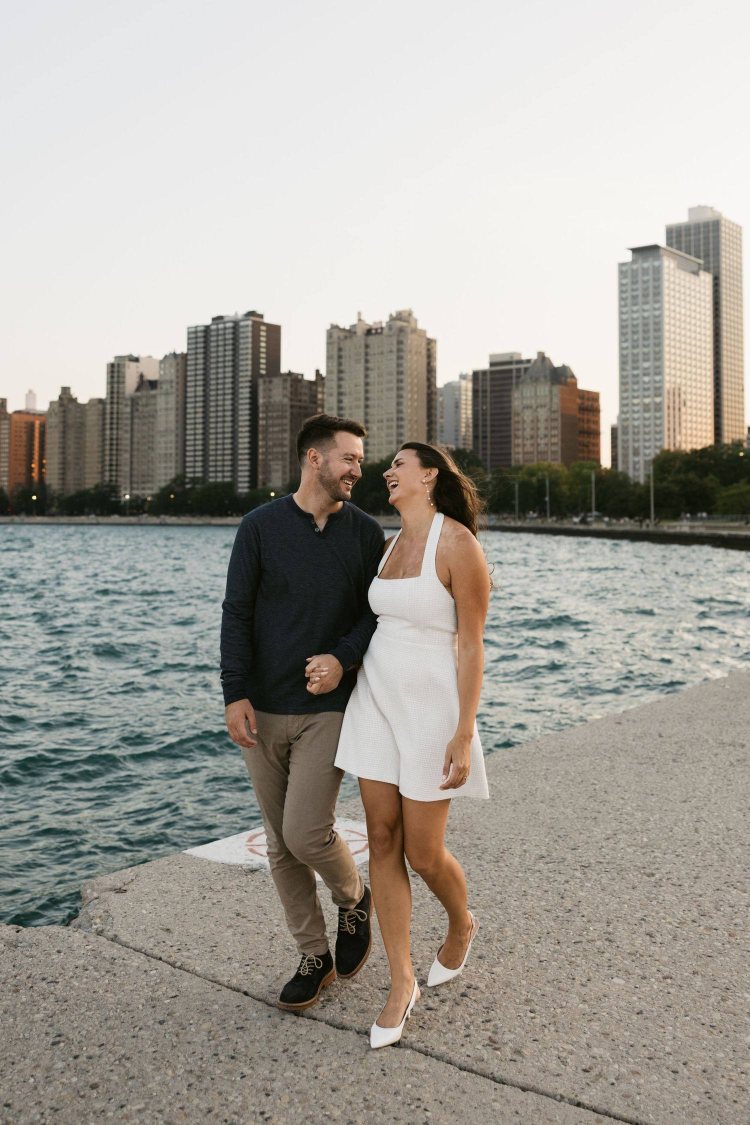 Romantic couple walking along Chicago lakefront with skyline backdrop at sunset.