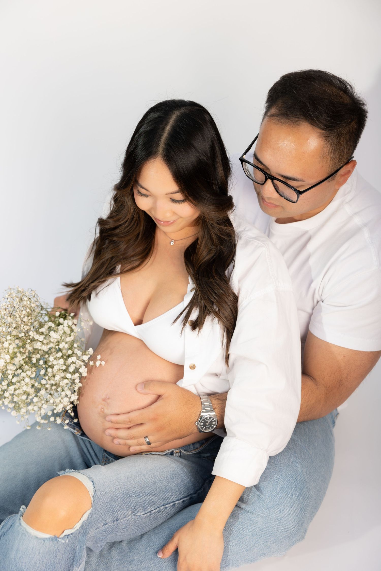 Couple sharing intimate moment during maternity photoshoot with baby's breath flowers.