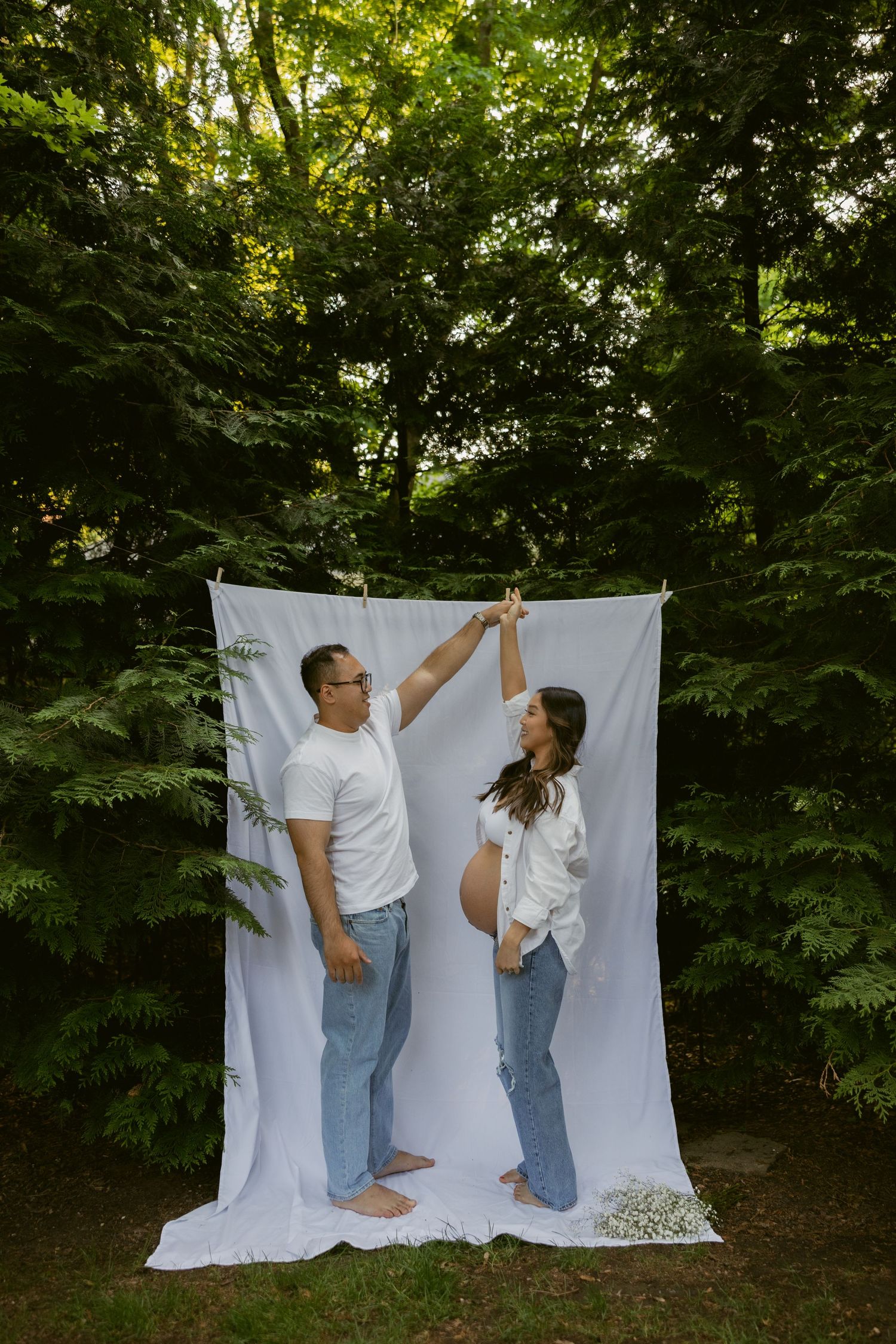 Outdoor couple's maternity session against white backdrop with natural greenery.
