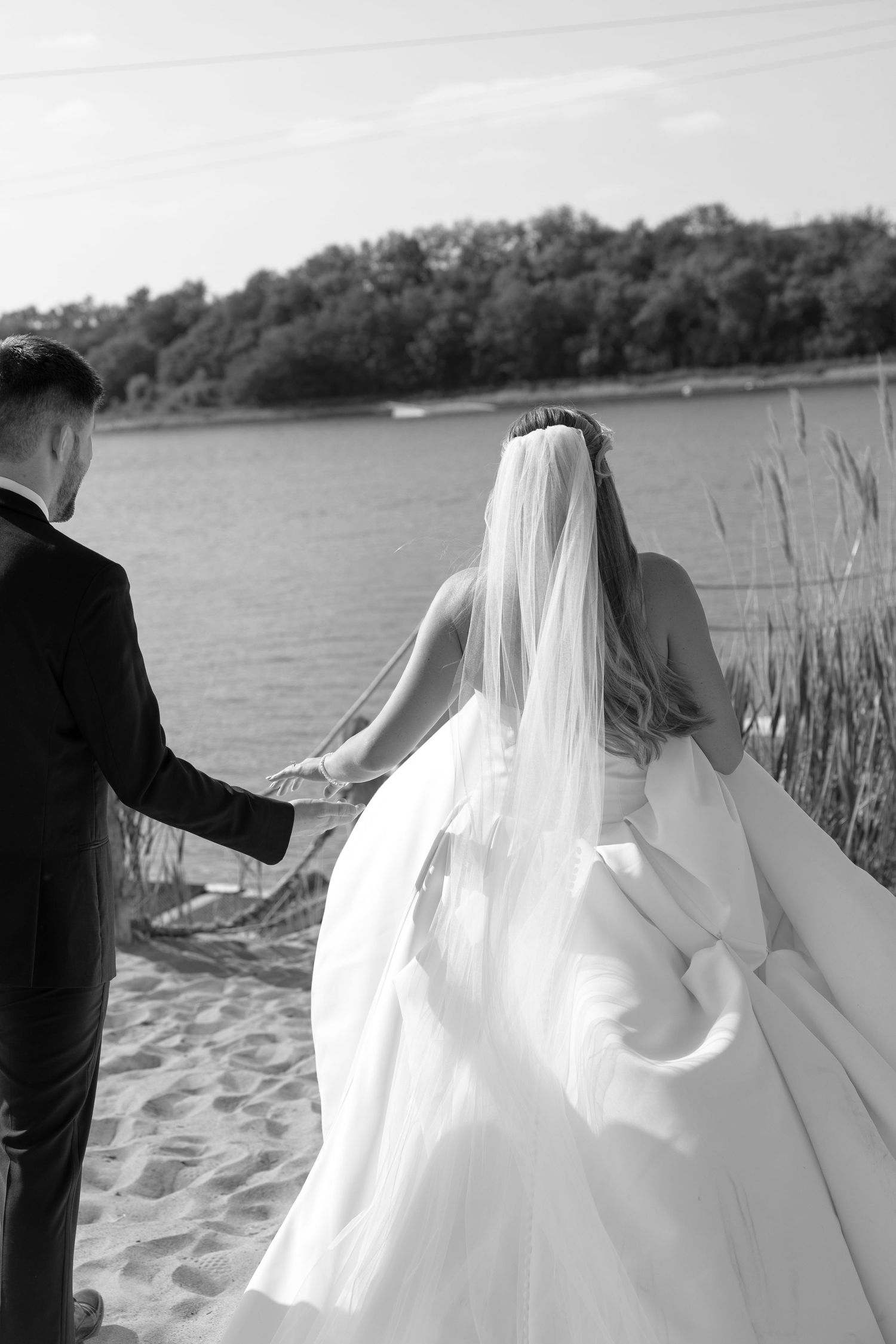 Black and white photo of couple walking along sandy beach shore with flowing wedding dress.