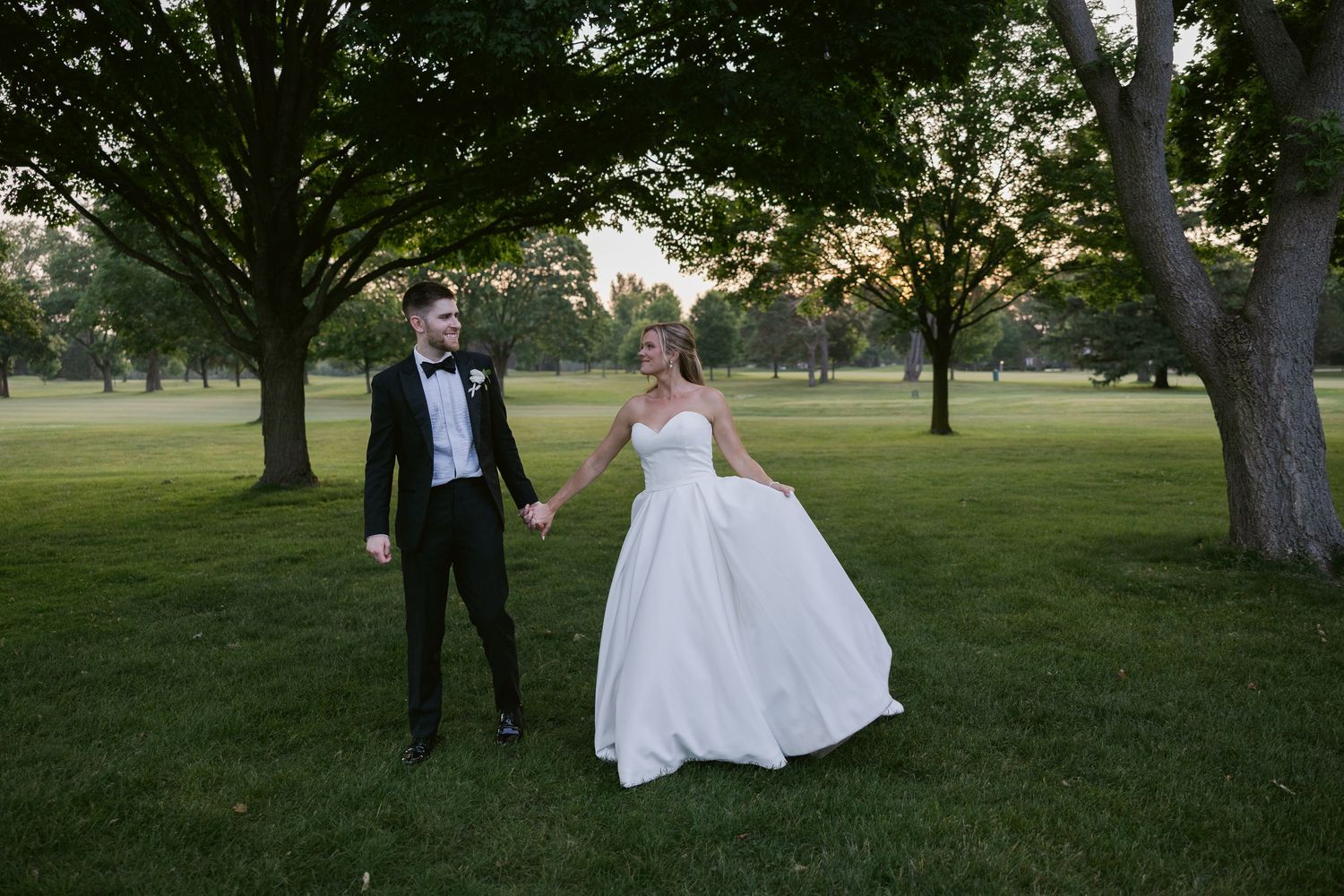 Couple dances together on green lawn during sunset wedding celebration.
