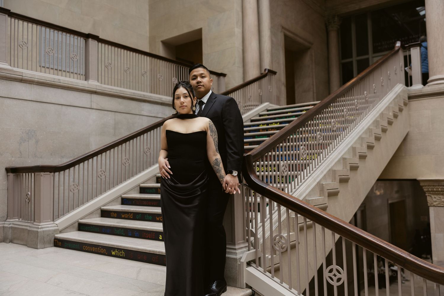 A couple poses on an elegant marble staircase in formal attire during a photoshoot.