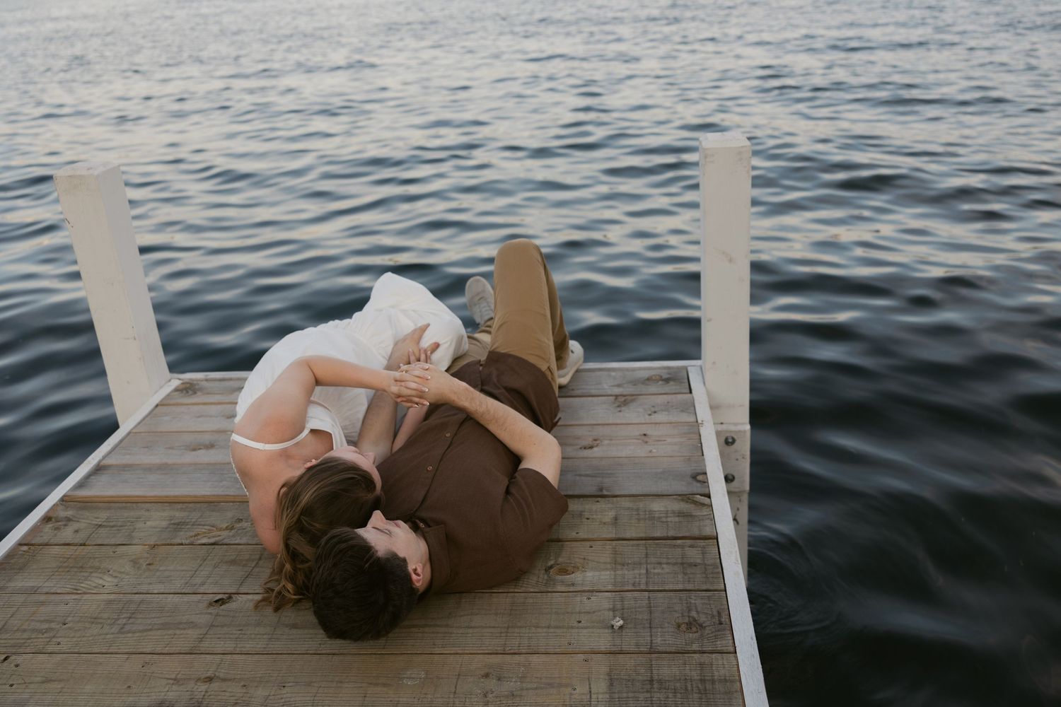 Person lying on a wooden dock overlooking calm water during sunset, creating a peaceful serene moment.