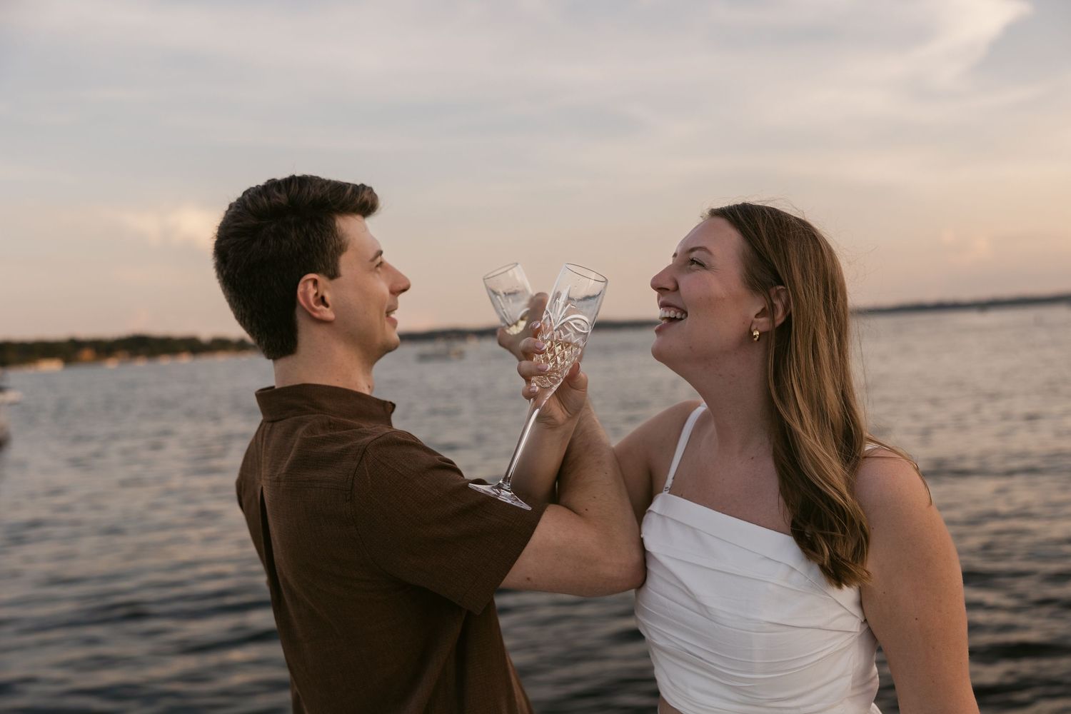 Couple sharing celebratory champagne toast on waterfront dock at dusk.