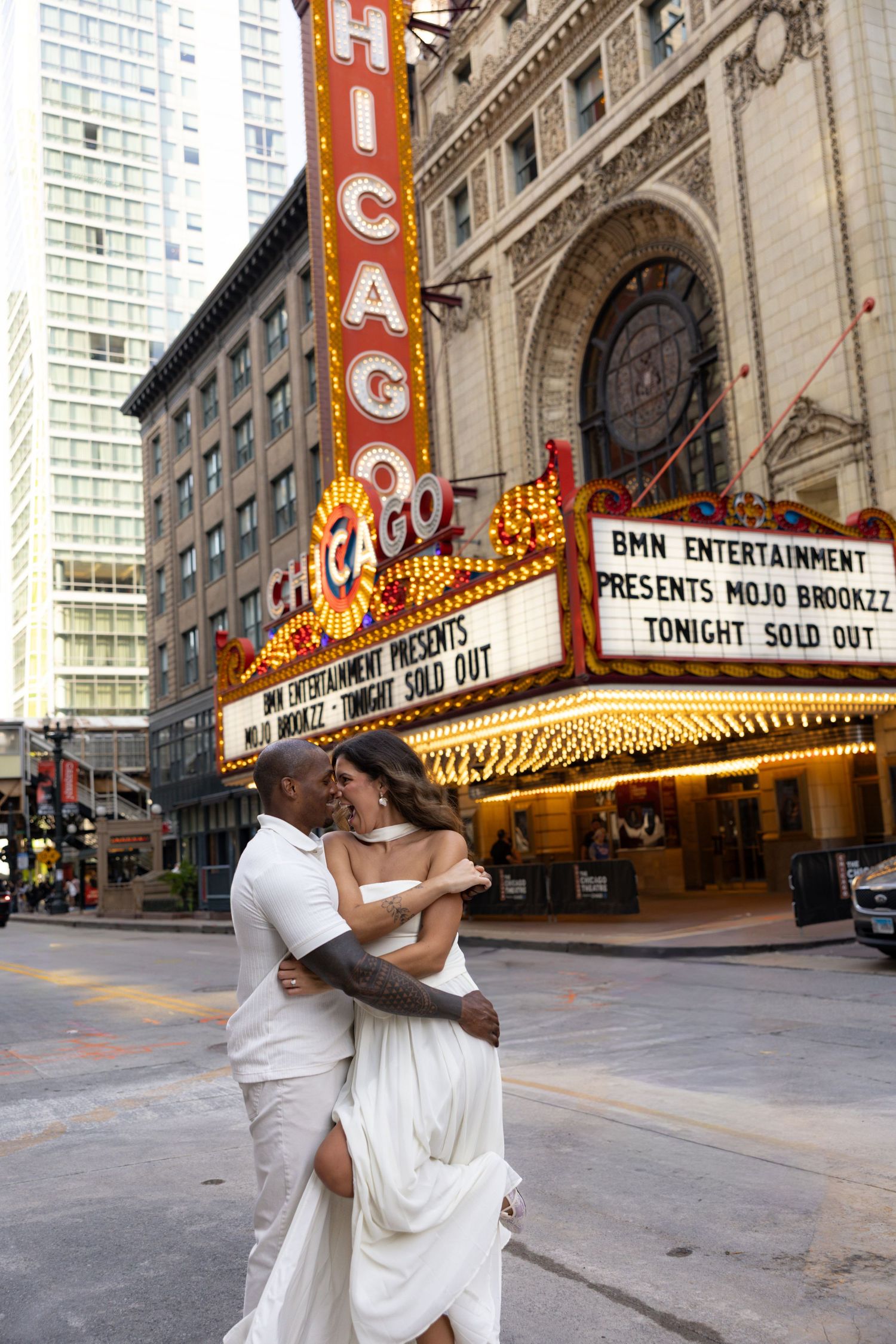 Couple shares intimate moment in front of iconic Chicago Theatre's bright marquee.
