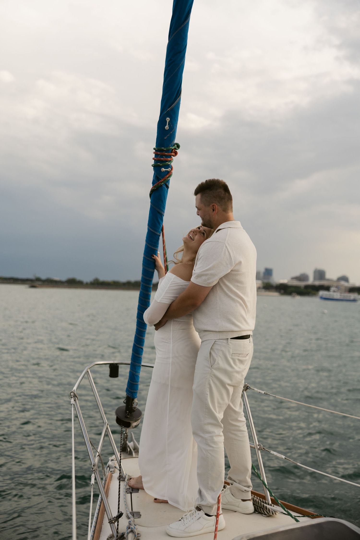 A couple in white clothing sharing a romantic moment on the deck of a sailing yacht.