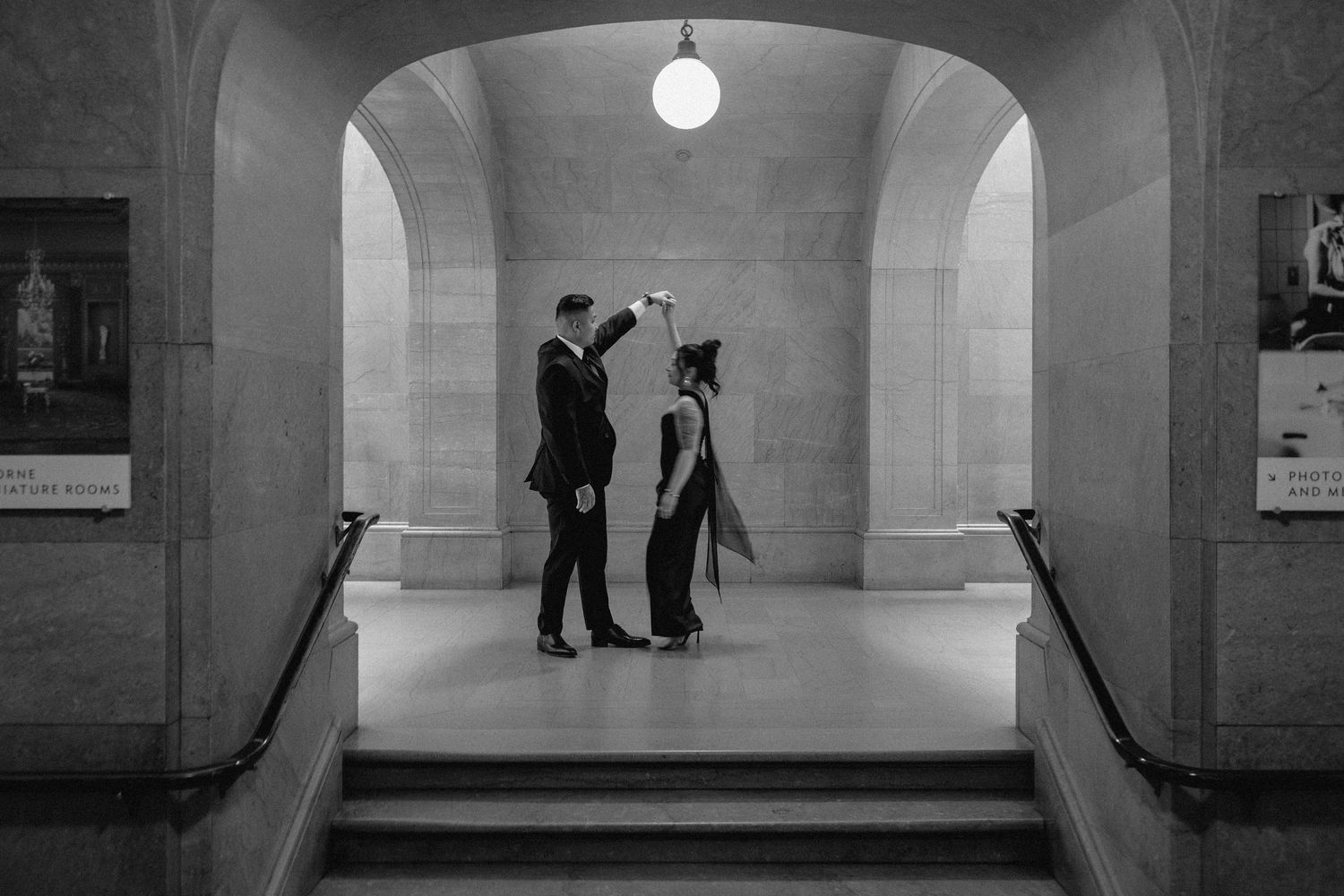 Three silhouetted figures stand in an arched hallway with stone walls and a hanging light fixture.