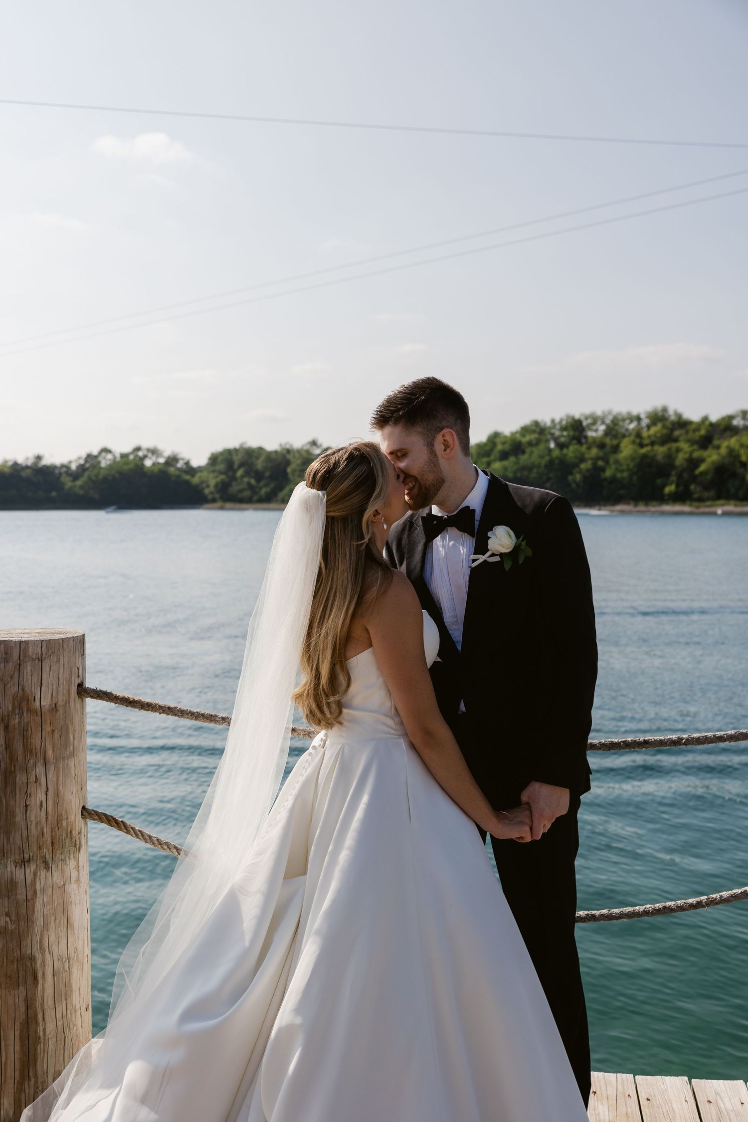 Romantic waterfront photo session with flowing white wedding dress against blue water backdrop.