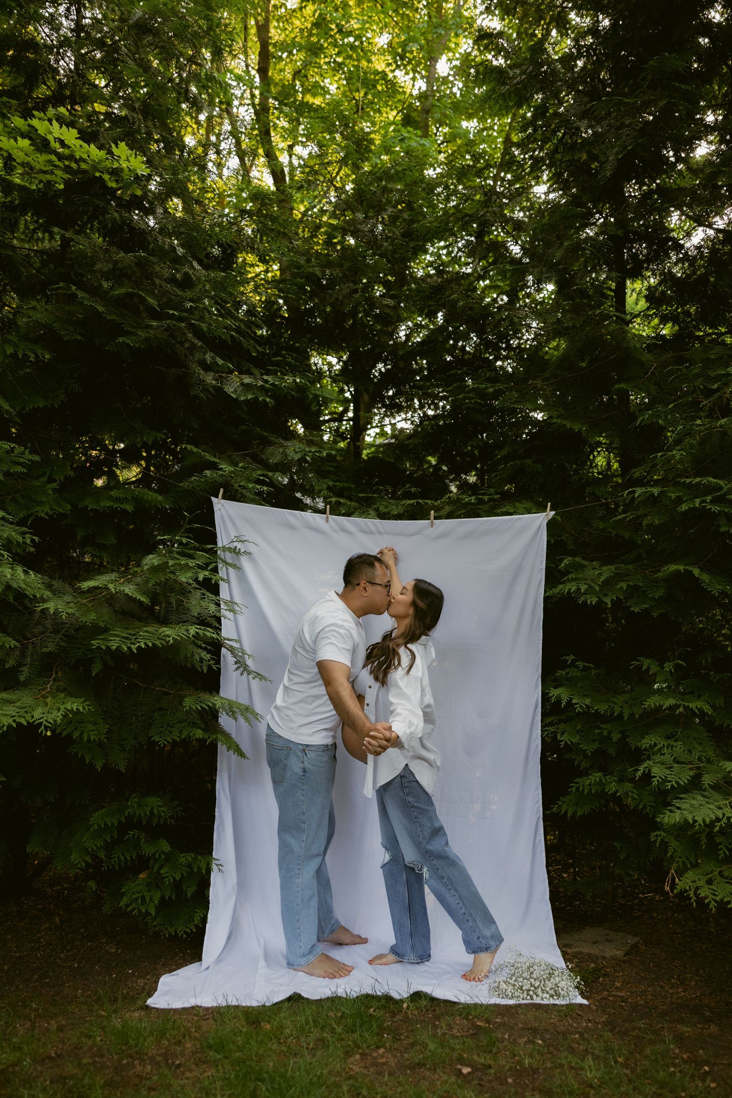 A romantic couple's photo session with a white backdrop outdoors surrounded by greenery.