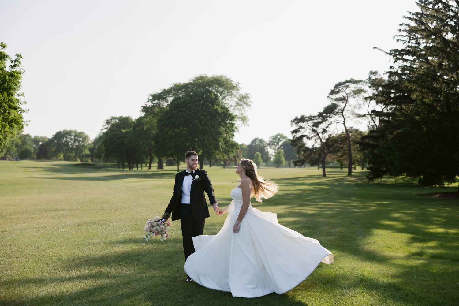 Elegant wedding couple walking across a sunlit golf course during golden hour.