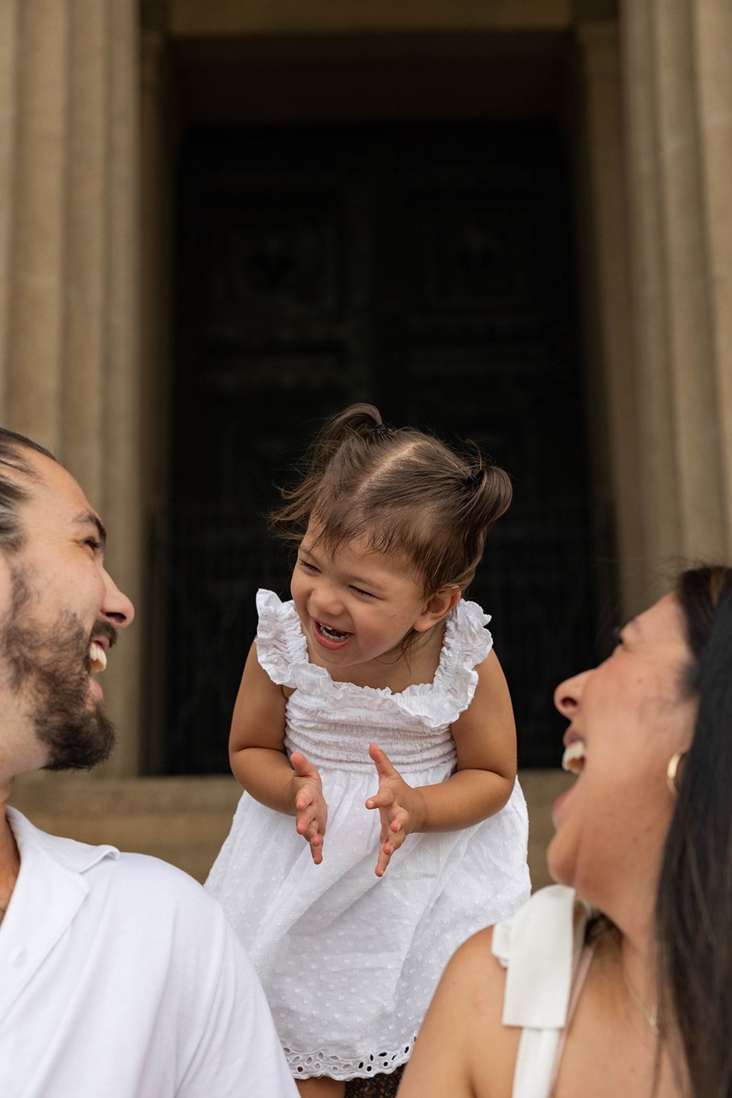 A heartwarming family moment showing shared laughter between three people by stone columns.