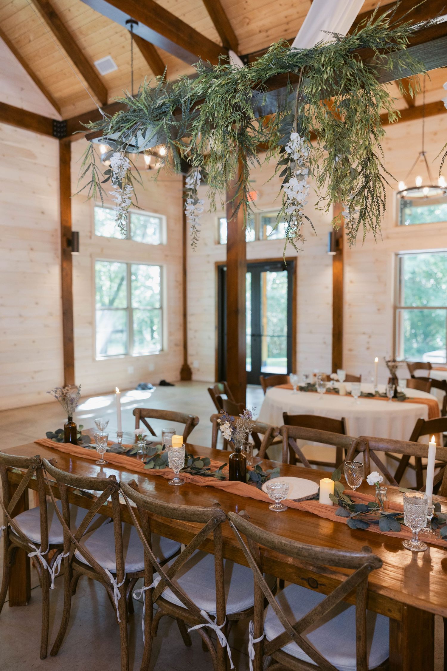 Rustic wedding reception venue with wooden tables and hanging greenery decorations.