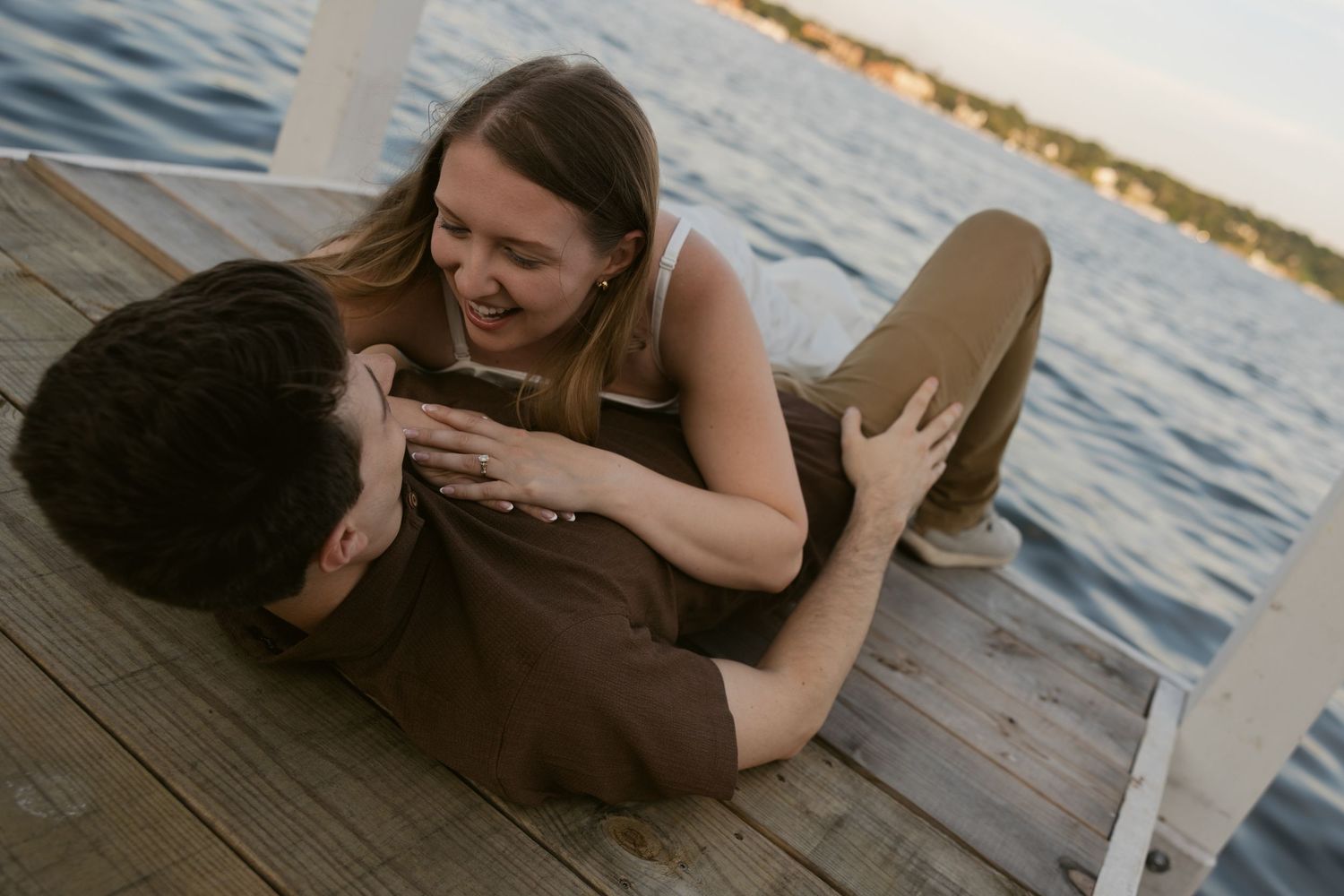 Two people lying together on a wooden pier overlooking a serene ocean at sunset, creating a romantic atmosphere.