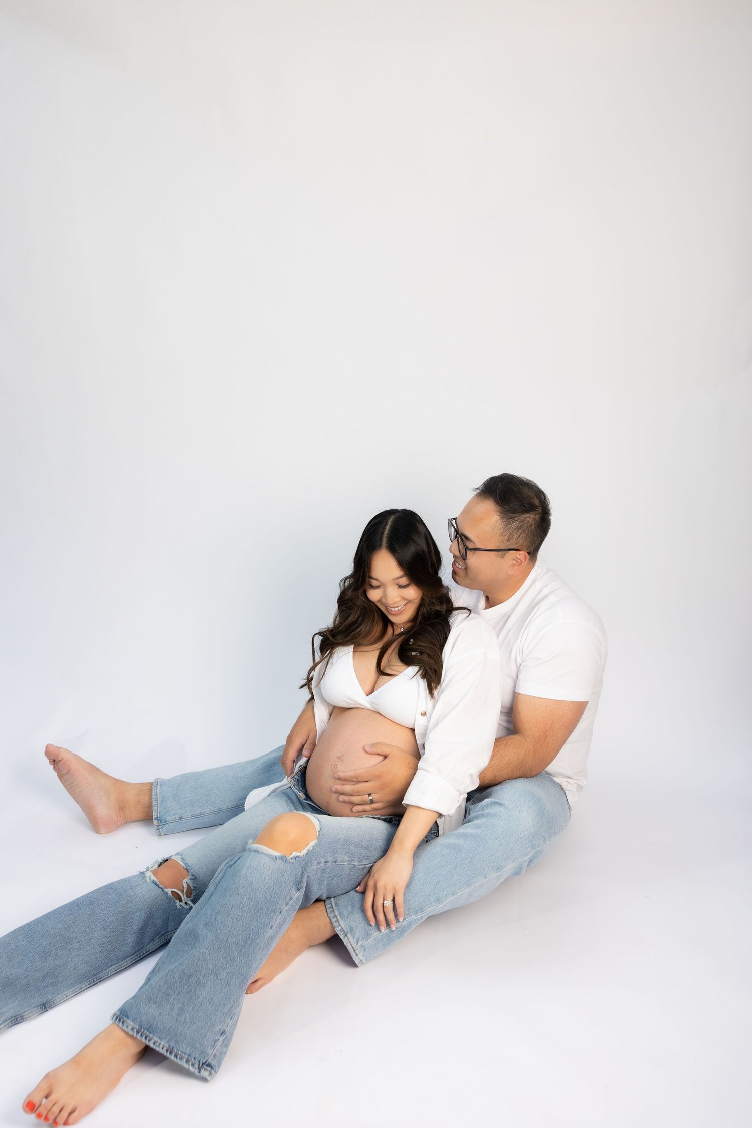 Intimate maternity portrait of couple sitting on floor in studio.