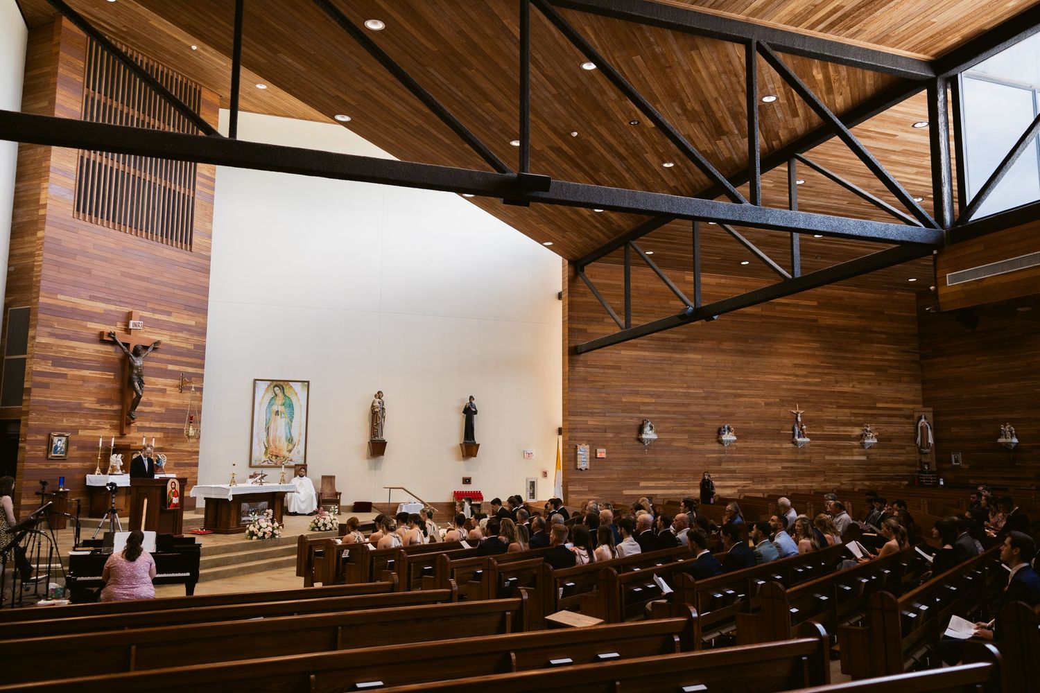 Wide angle view of wedding ceremony in a modern church with wooden interior and pews.