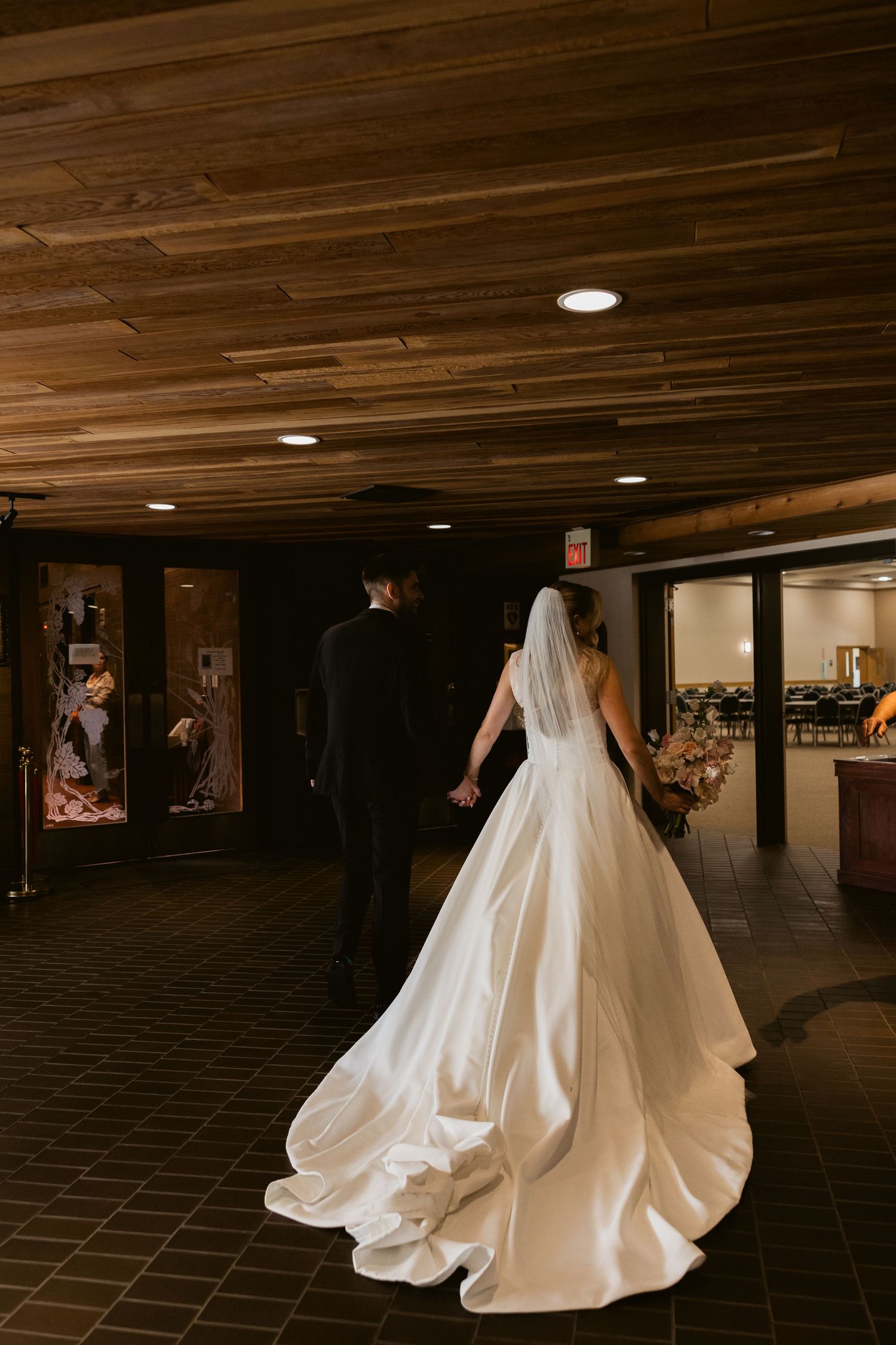 Bride in flowing white dress walking through a wood-paneled hallway.