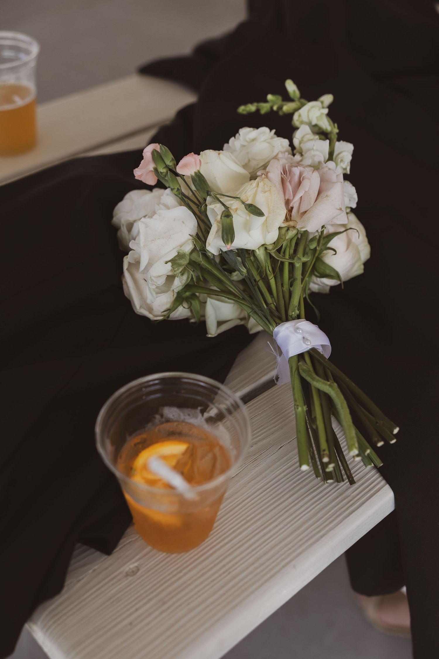 White floral arrangements in glass vases next to cocktails on a textured gray surface.