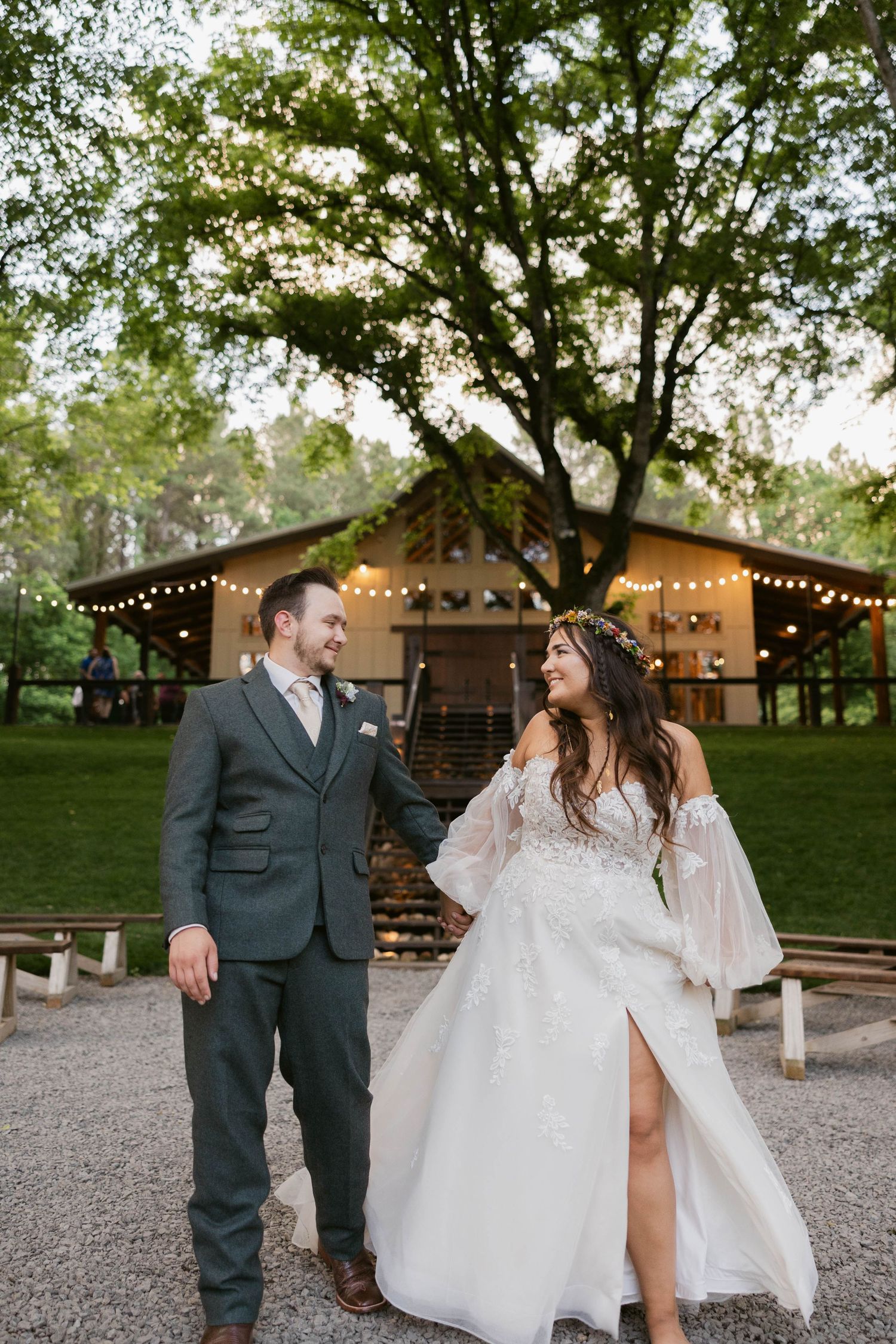 Newlyweds share intimate moment outside rustic venue with string lights at dusk.