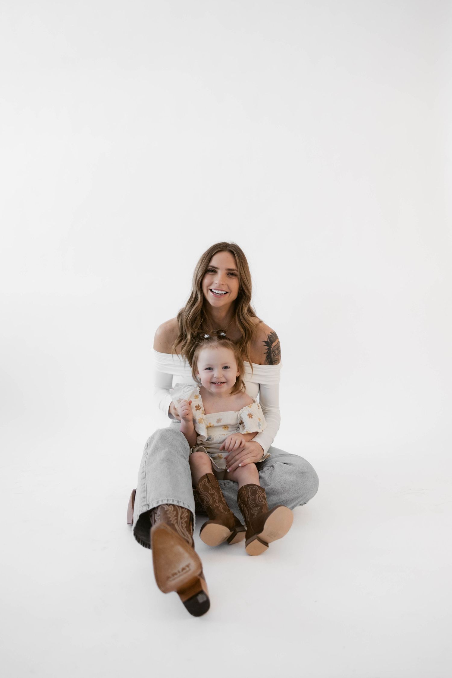 Parent and child sit together wearing casual attire against clean white background.
