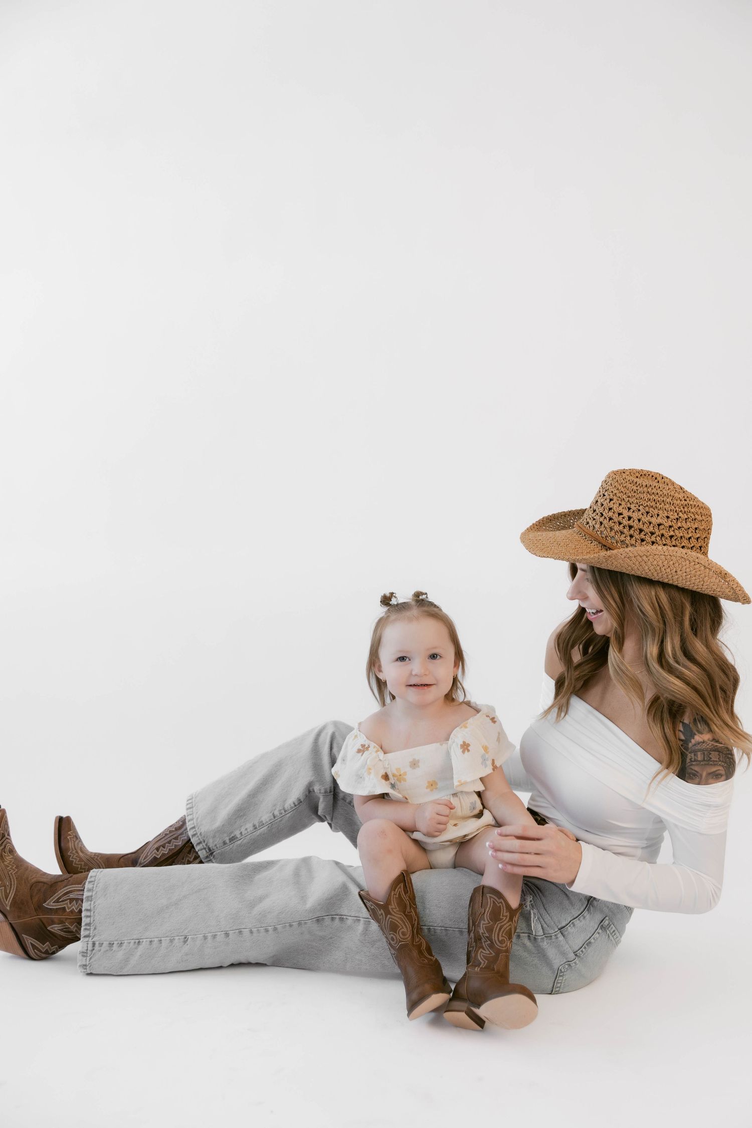 Parent and child share tender moment while lying on white studio floor wearing boots and denim.
