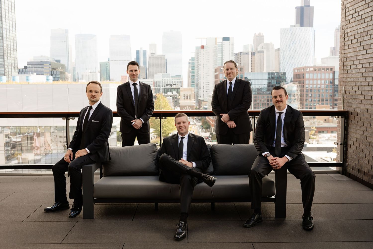 Wedding party members in formal attire gather near large windows with cityscape backdrop.