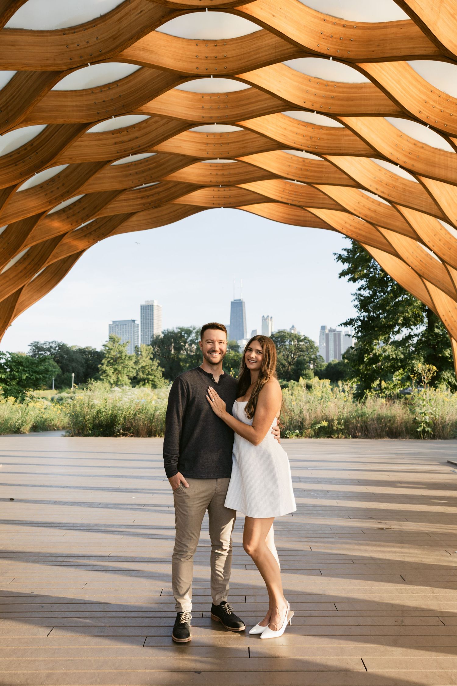 Couple poses under a modern wooden pergola with Chicago skyline visible in the background.