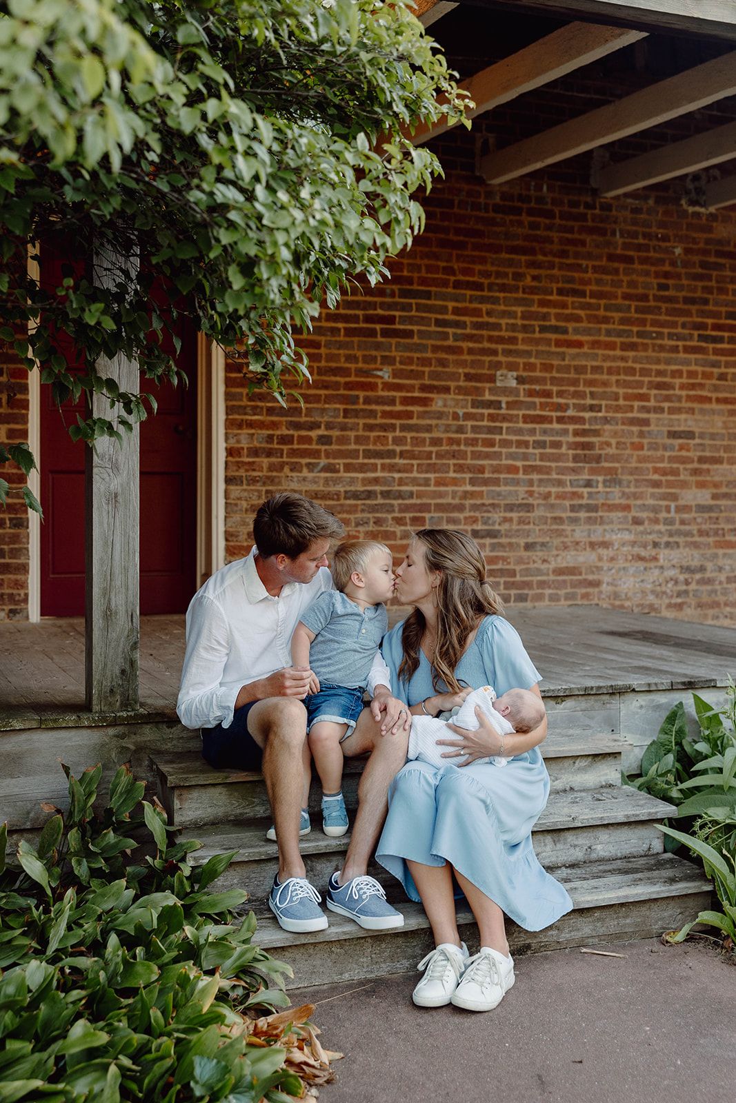 A family shares an intimate moment on brick steps surrounded by greenery.