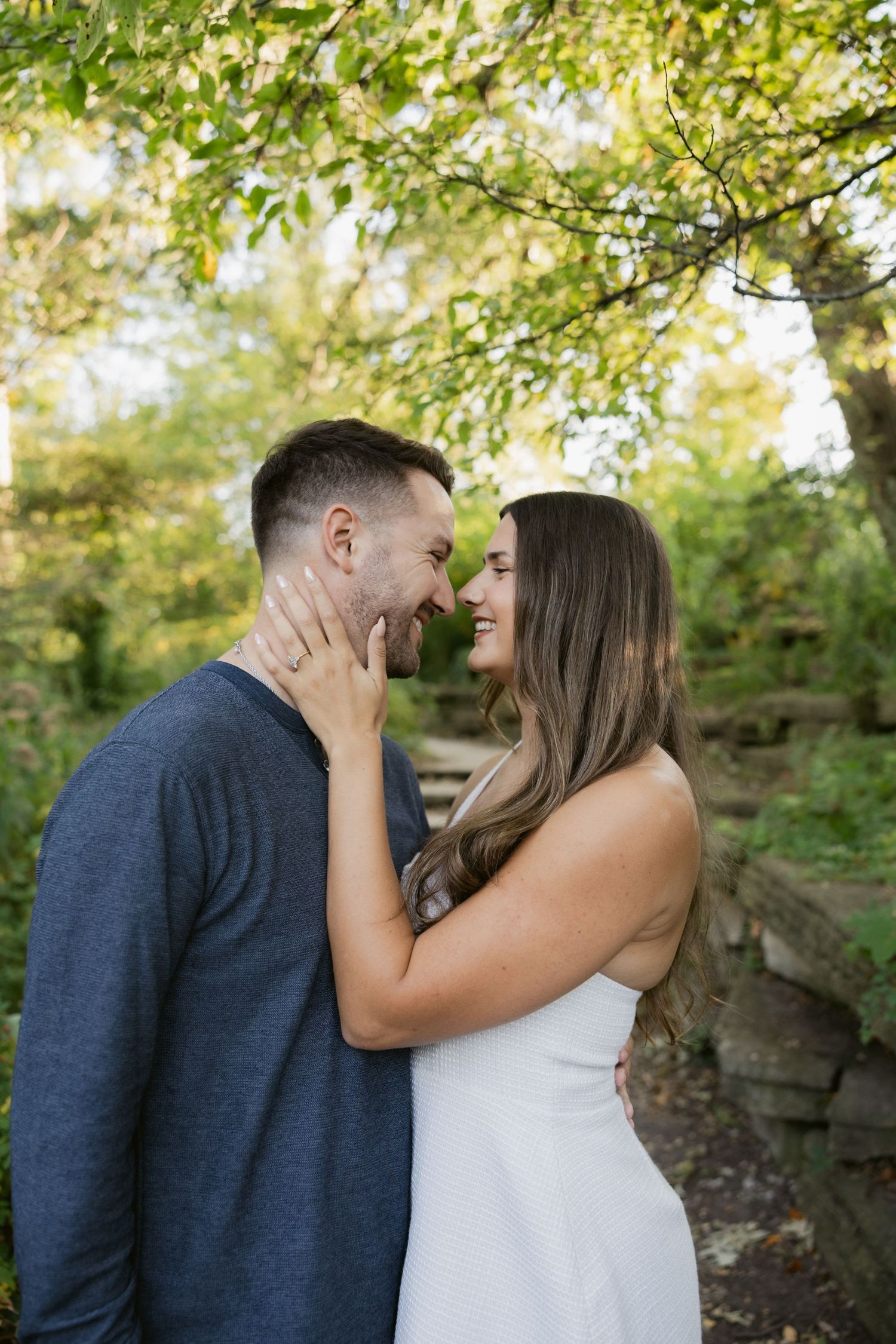 Intimate couple laughing together on a nature trail surrounded by green foliage.
