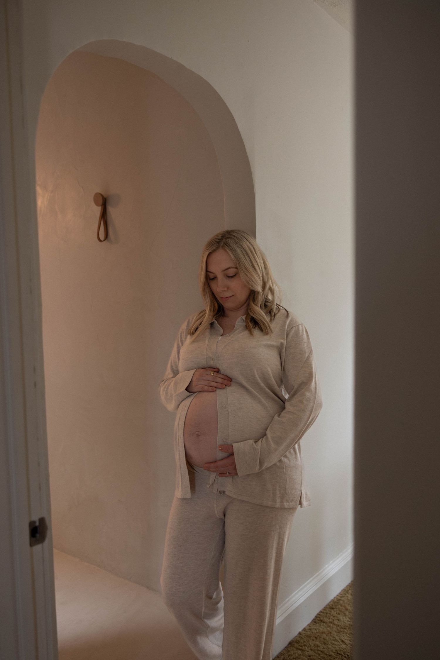 A serene maternity moment captured in an arched doorway with soft natural lighting.