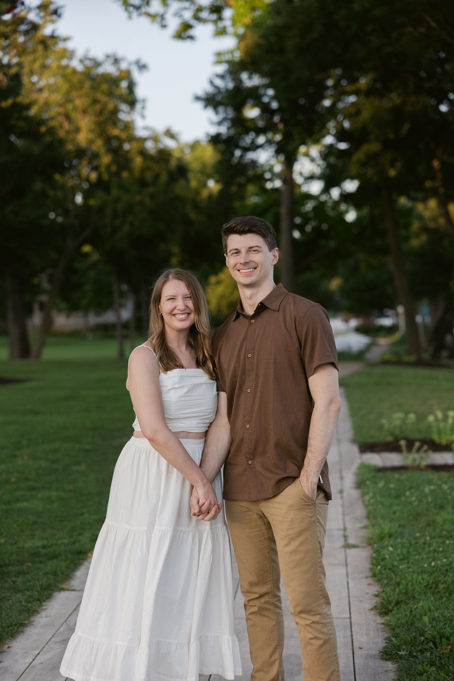 A happy young couple stands together on a garden path during a casual outdoor photo session.