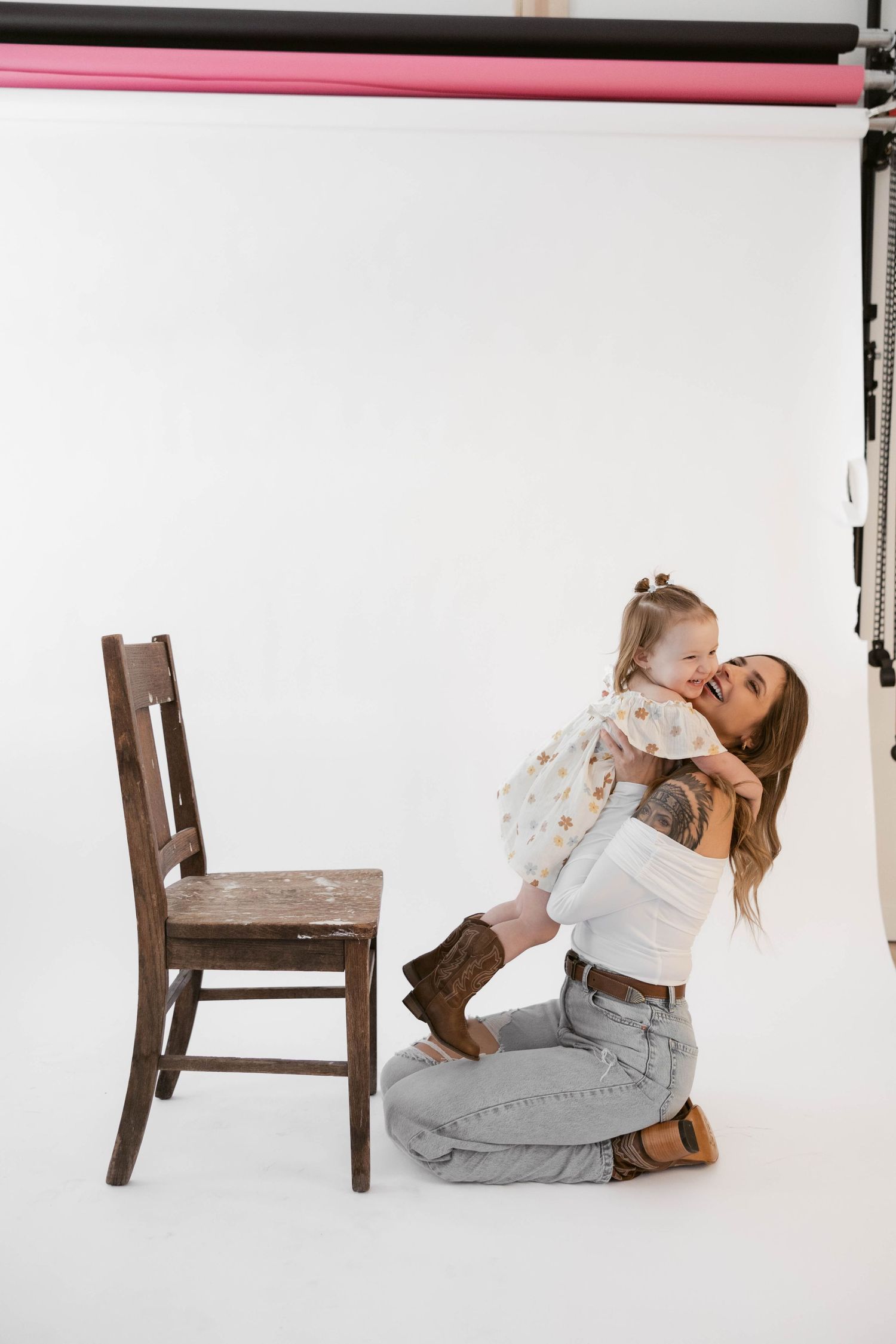 Candid studio moment showing joyful interaction beside wooden chair on white background.