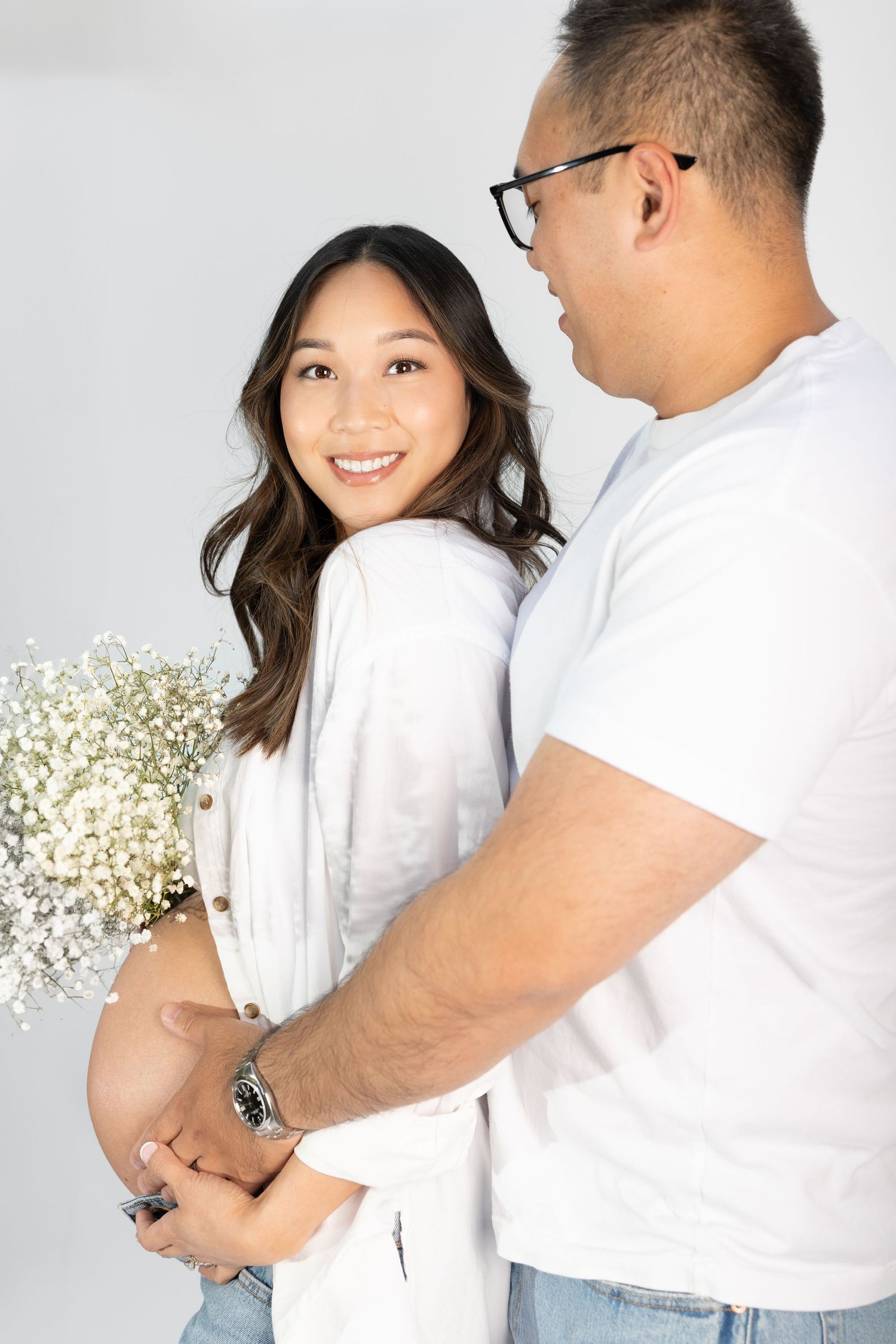 Expectant couple sharing tender moment with baby's breath flowers in studio setting.