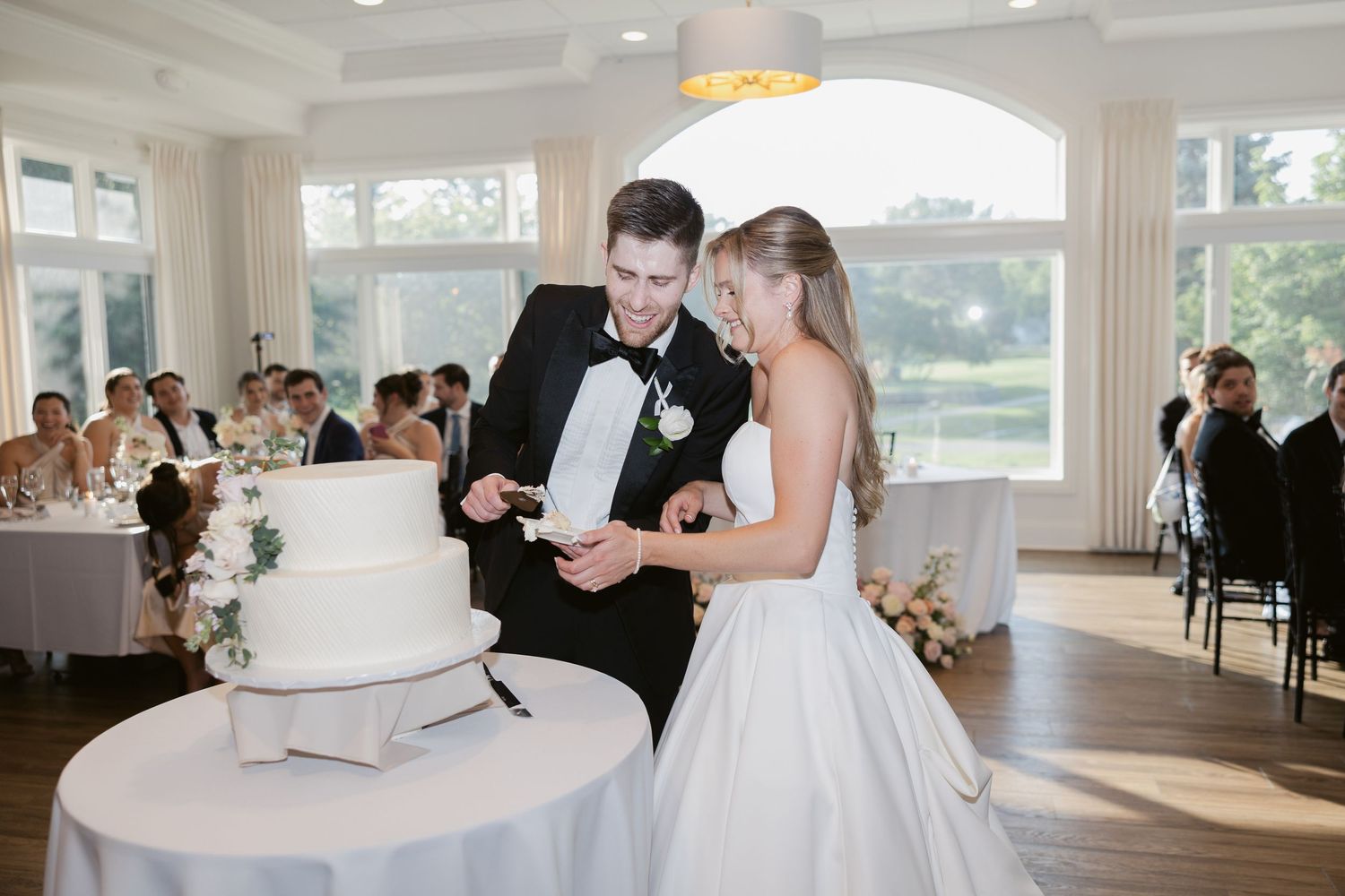 Wedding couple cuts their elegant white tiered cake during reception.