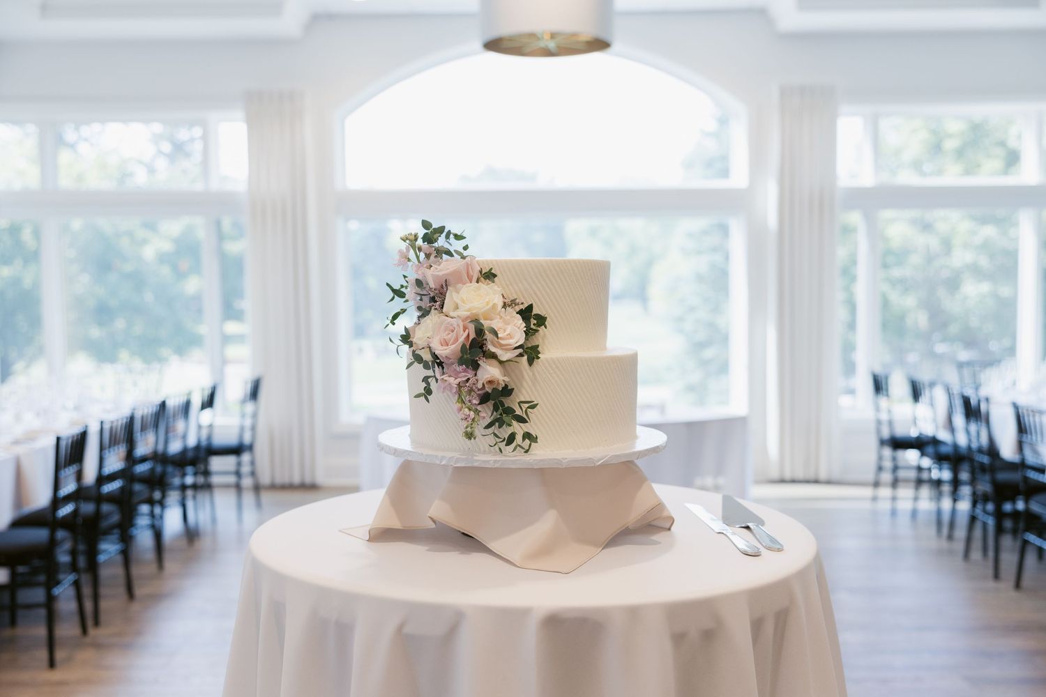 Elegant white wedding cake with pink floral decorations on a round table.