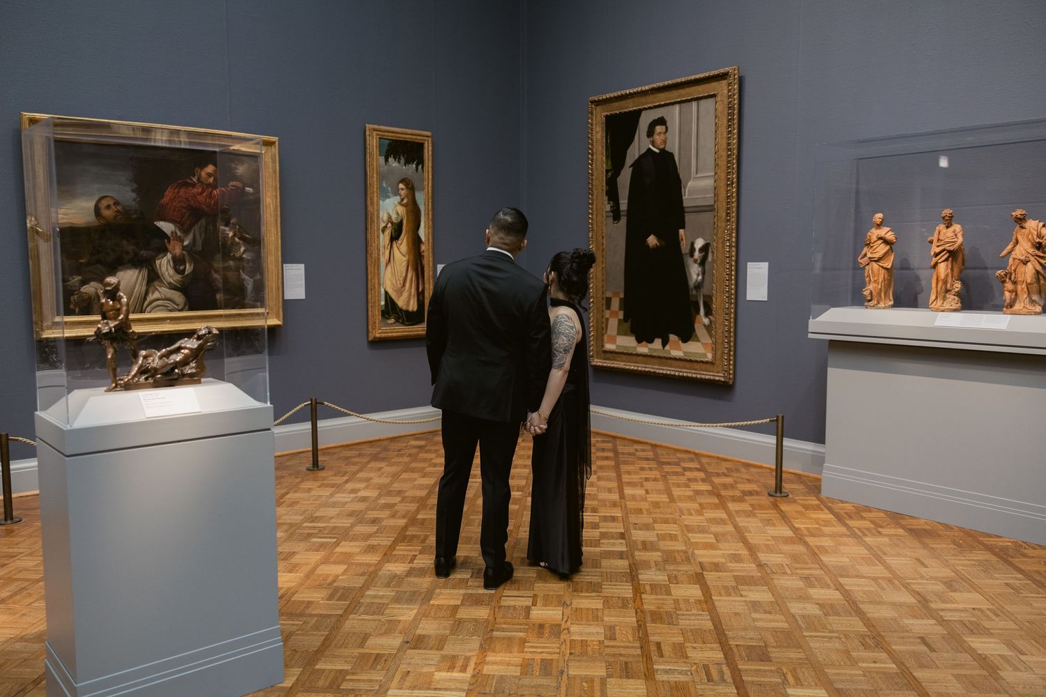 Interior view of an art museum gallery showing multiple framed paintings on blue-grey walls.