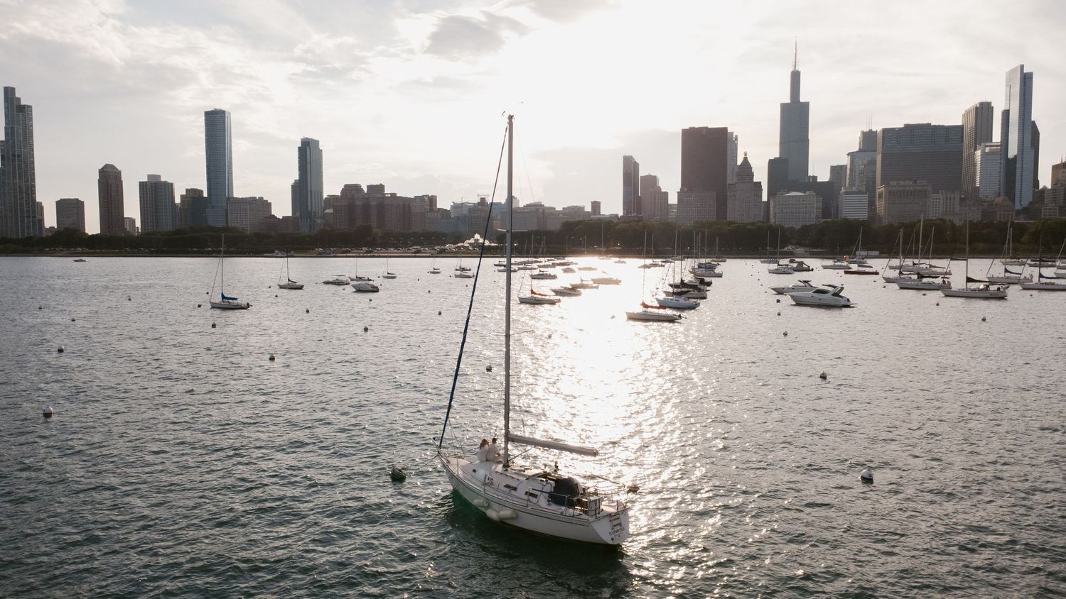 Wide panoramic view of boats dotting the harbor with city skyline in the distance.