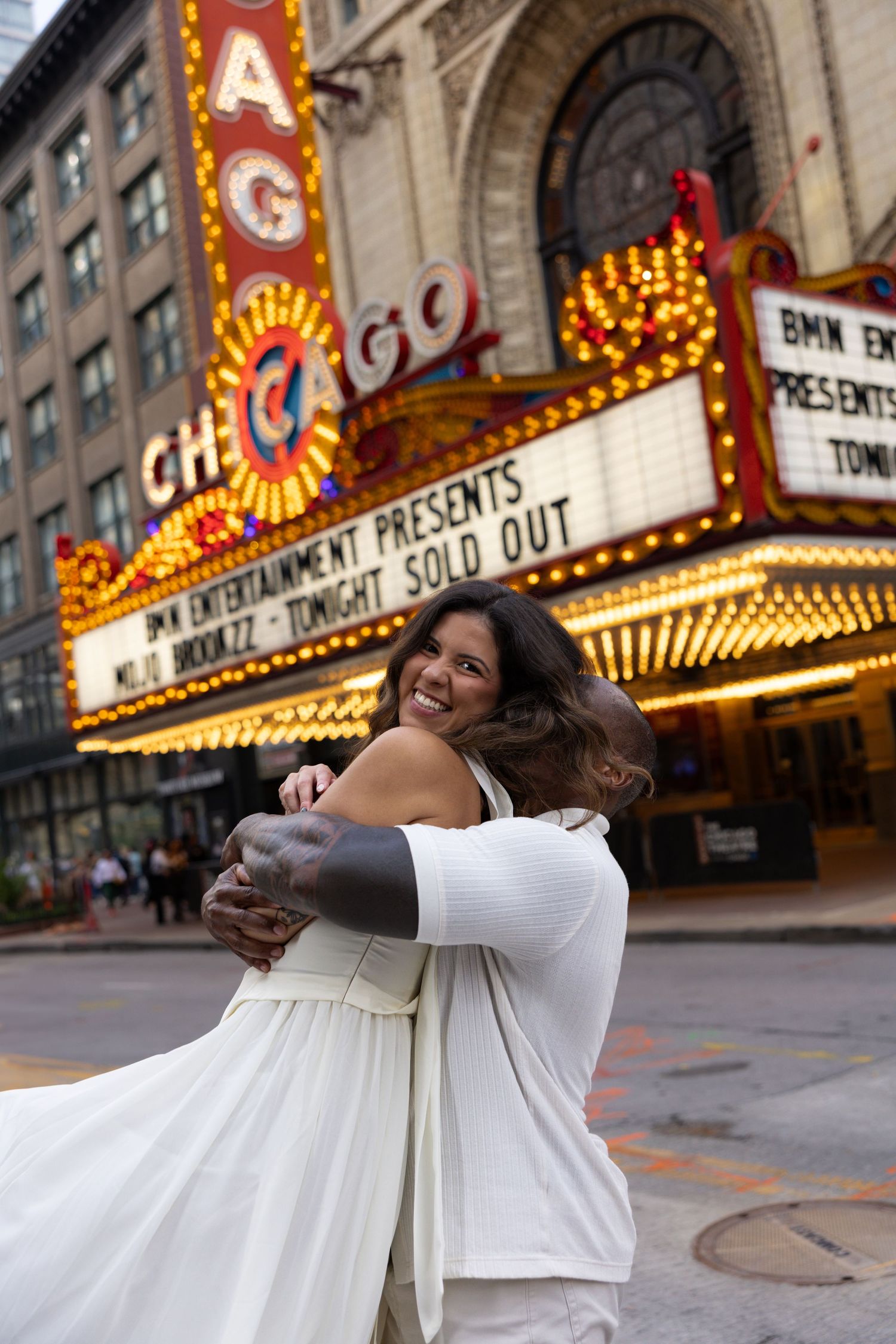 A couple shares a joyful embrace in front of the Chicago Theatre's bright marquee lights.