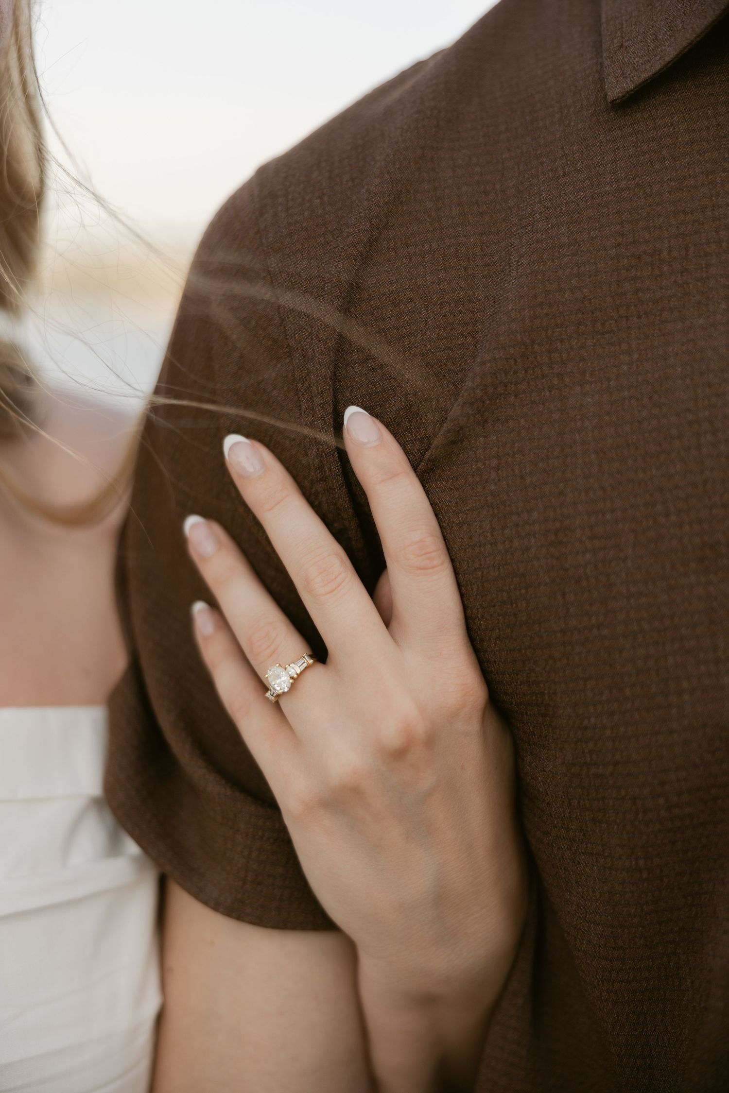 A close-up shot of an engagement ring on someone's hand against a brown sweater background.