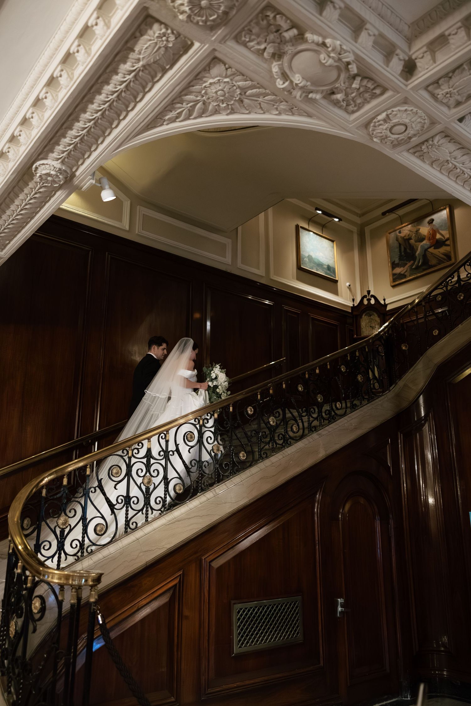 An ornate staircase with wrought iron railings and decorative ceiling moldings in a classic wedding venue.