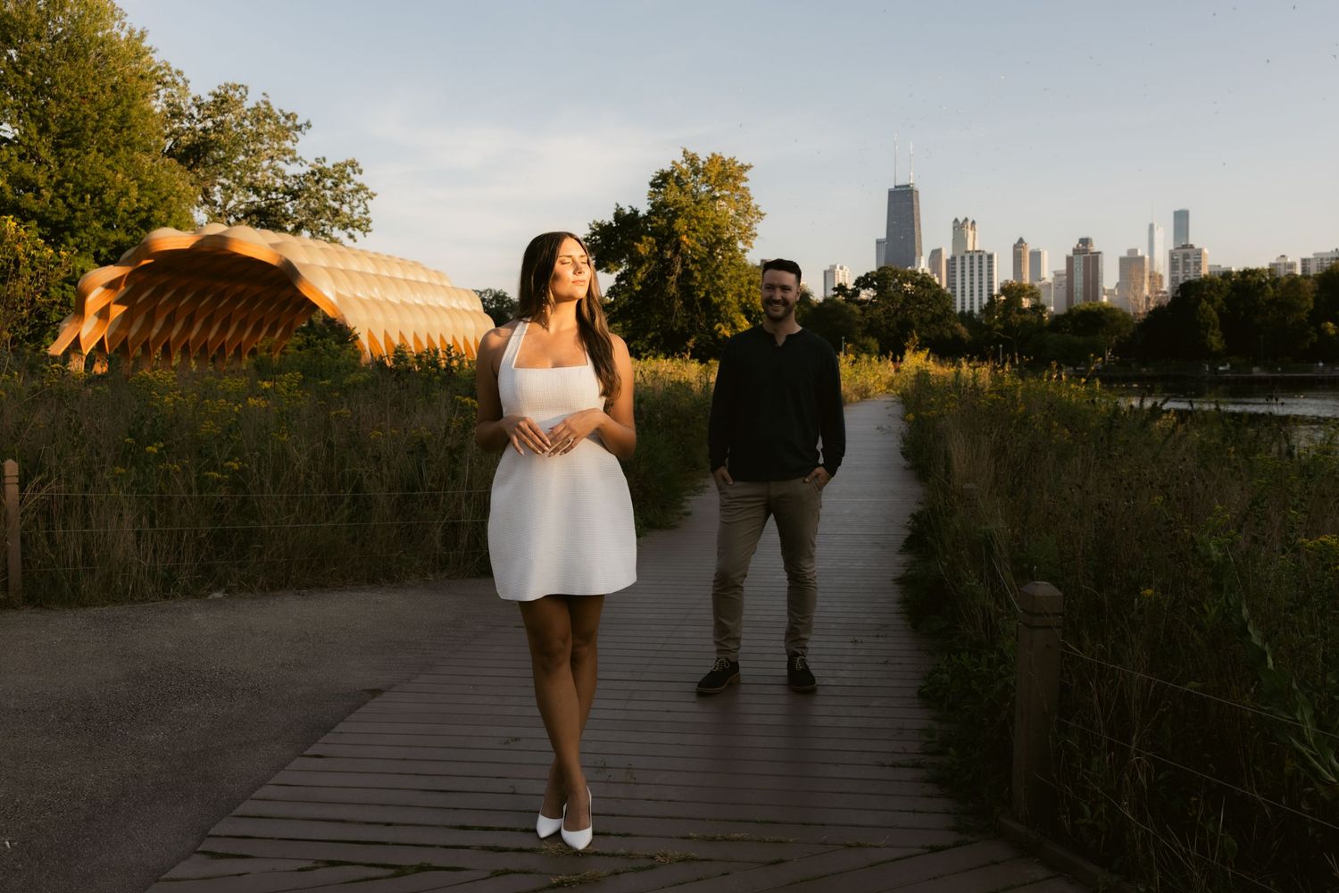 A scenic walkway path along a grassy urban waterfront with the Chicago skyline visible in the distance at sunset.