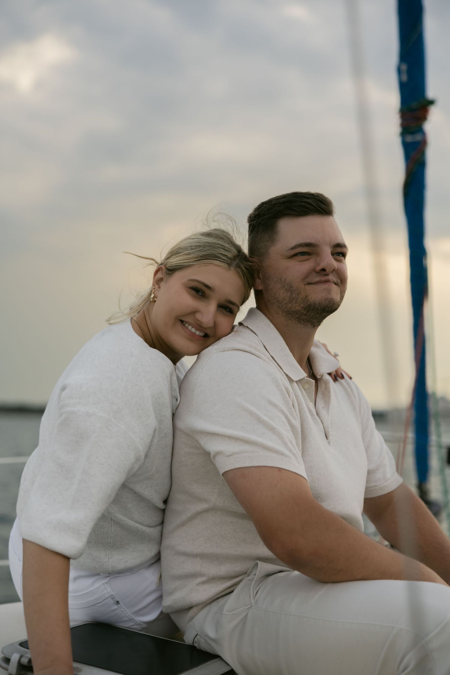 A romantic couple wearing white outfits share intimate moments on a boat with a city skyline in the background.