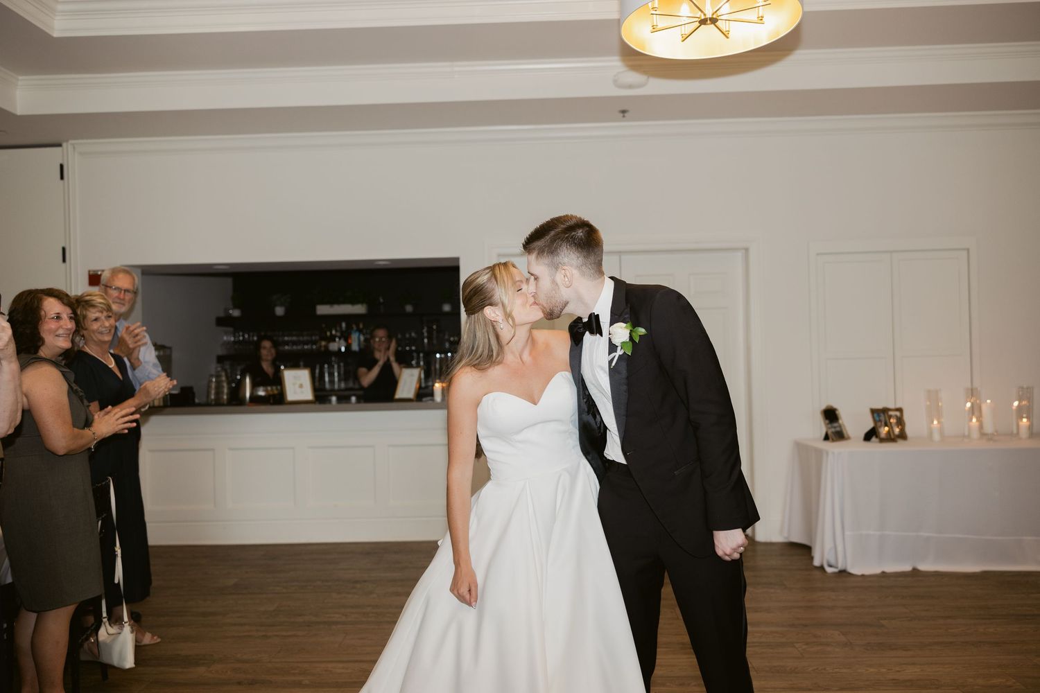 A couple shares their first dance in an elegant white reception room with hardwood floors.