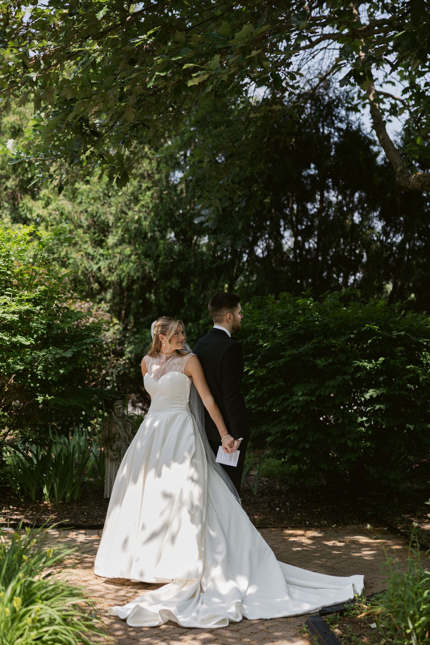 A bride in a flowing white gown poses gracefully in a lush garden setting during a wedding photoshoot.