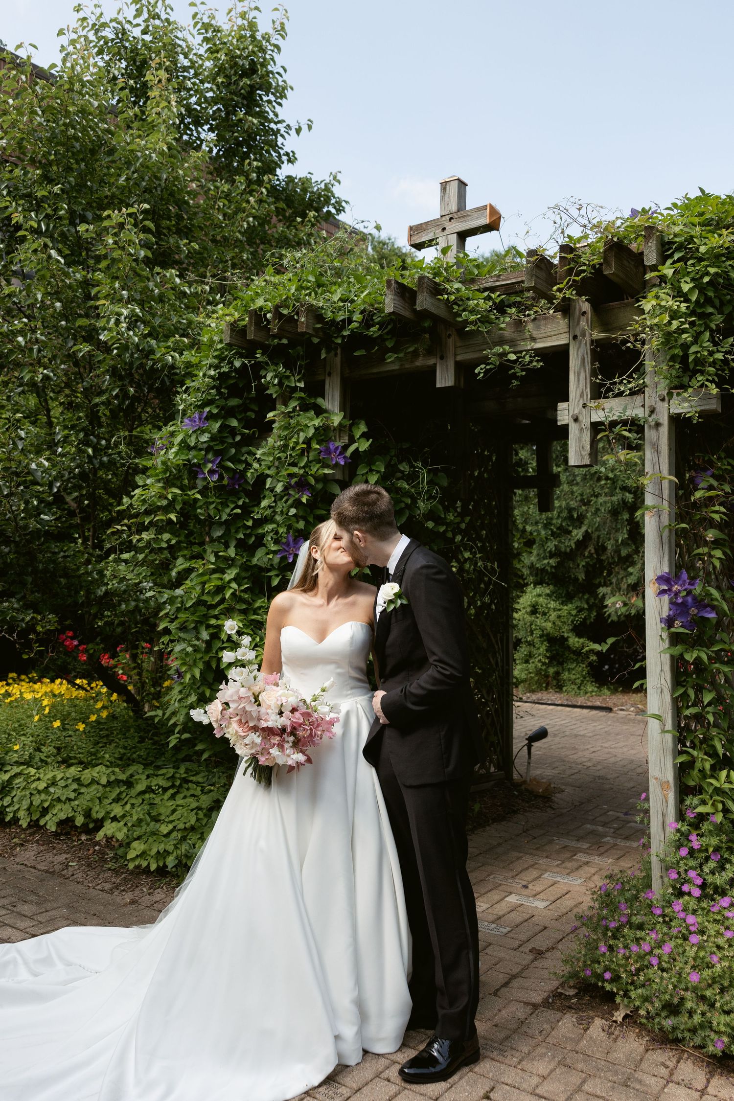 Newlyweds sharing an intimate moment under a cross-adorned garden arbor.
