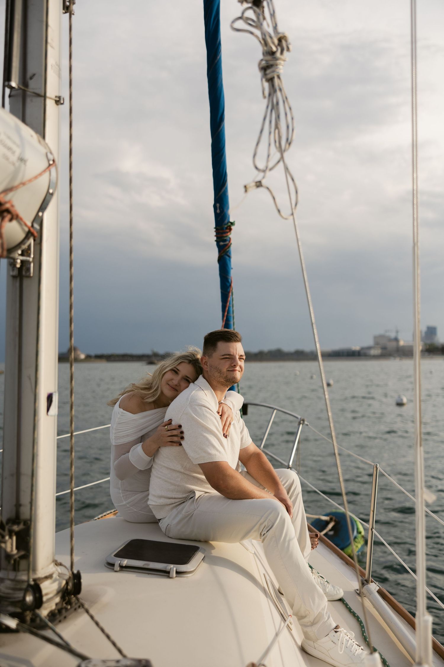 A romantic couple in white outfits sharing an intimate moment while sailing on a yacht during sunset.