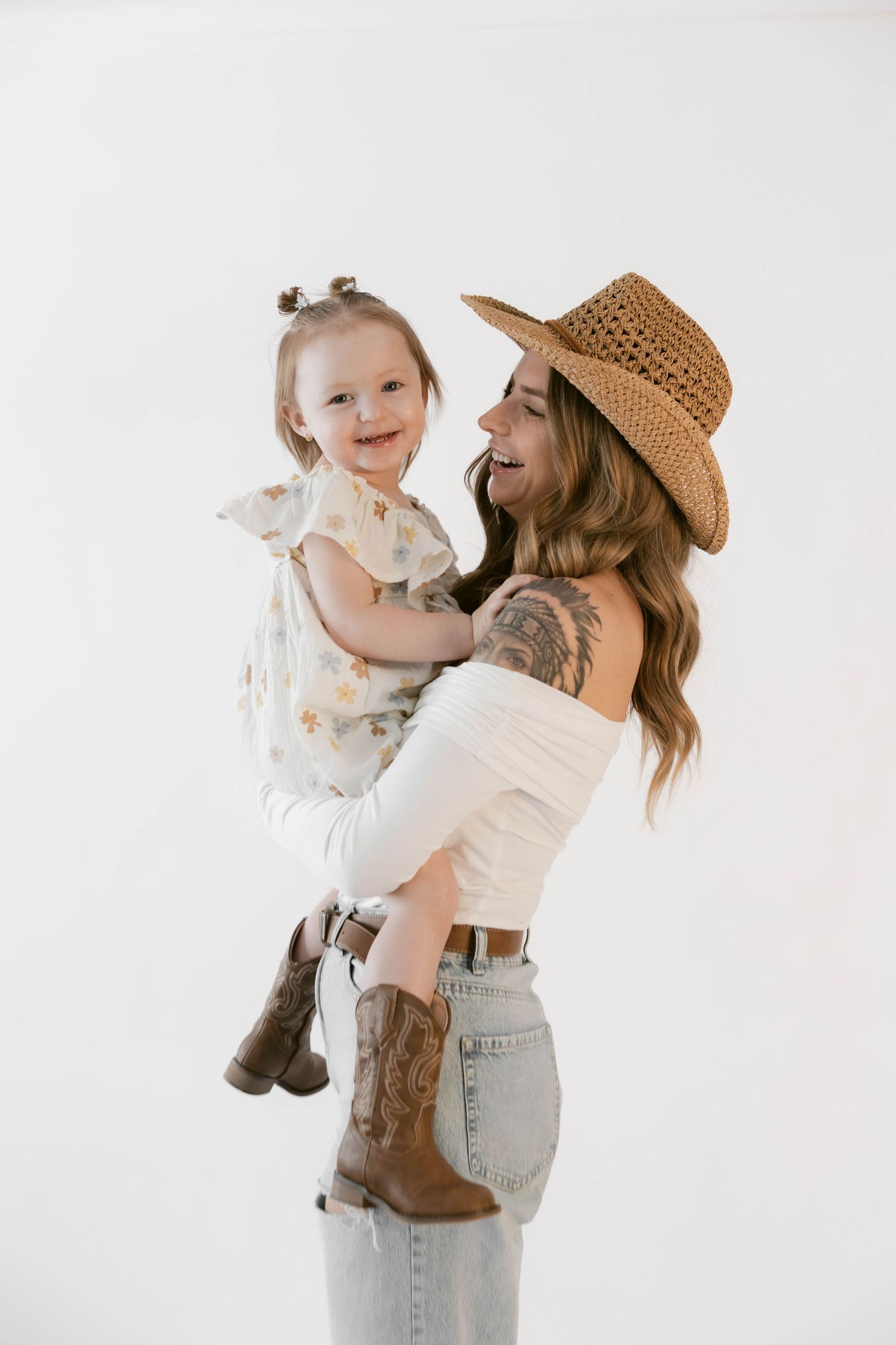 A western-styled photo shoot against white backdrop shows playful interaction while wearing cowboy boots and a straw hat.