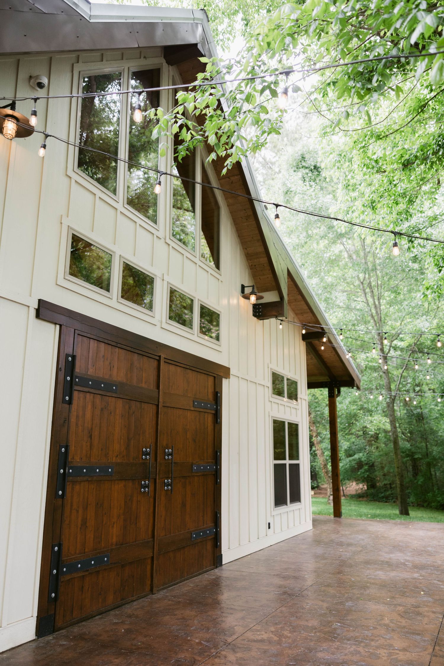 Modern rustic wedding venue exterior with large wooden doors and string lights.
