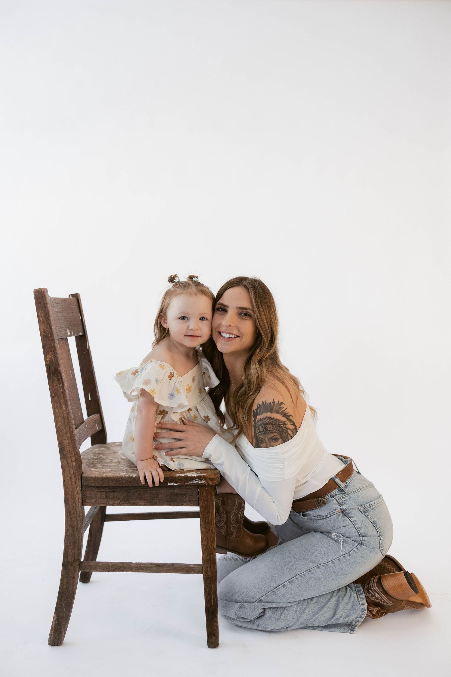 Studio portrait with wooden chair showing warm embrace against clean white backdrop.