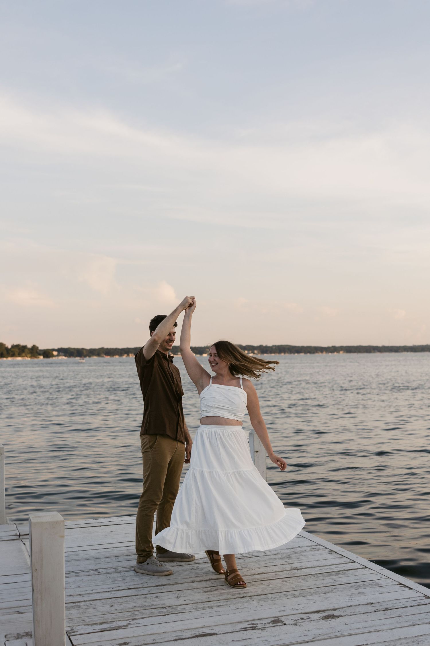 Romantic couple sits together on a wooden dock overlooking a serene lake at sunset.