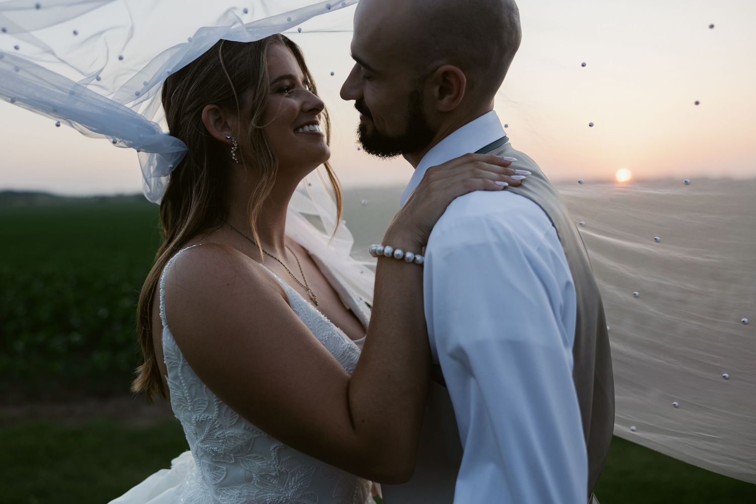 A happy couple shares a romantic sunset moment while celebrating their outdoor wedding in a beautiful field.